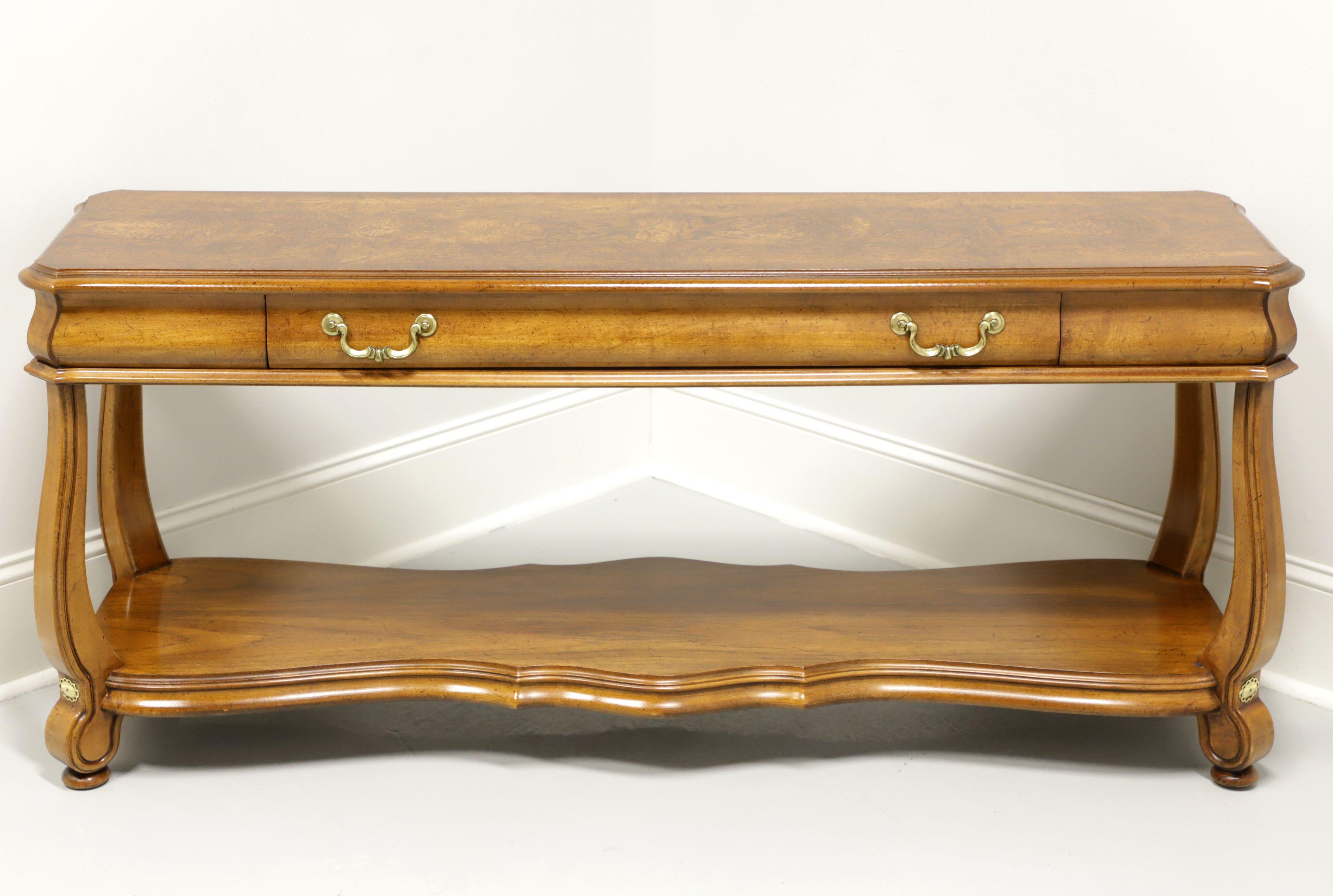A Transitional style sofa table by Gordon's Furniture, of Johnson City, Tennessee, USA. Solid oak with burl oak top, brass accents & hardware, serpentine shaped undertier shelf, curved legs and flat bun feet. Features one drawer of dovetail