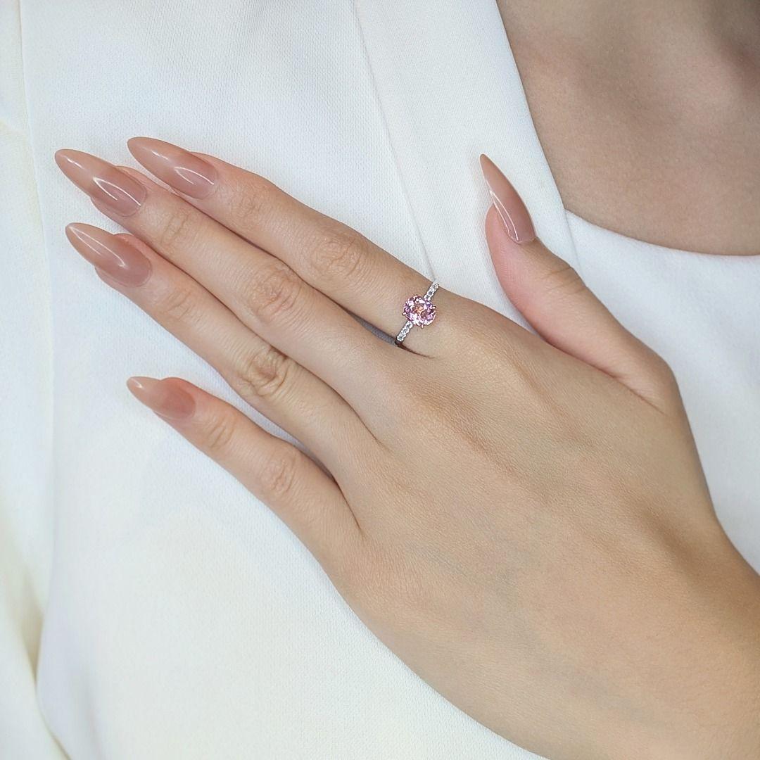 Cette magnifique bague pave de 1,55ct est ornée en son centre d'une tourmaline rose ovale de 1,5ct, d'un éclat doux et radieux, à la fois vibrant et élégant. La bague est également rehaussée de 10 saphirs ronds et brillants, totalisant 0,05ct, qui