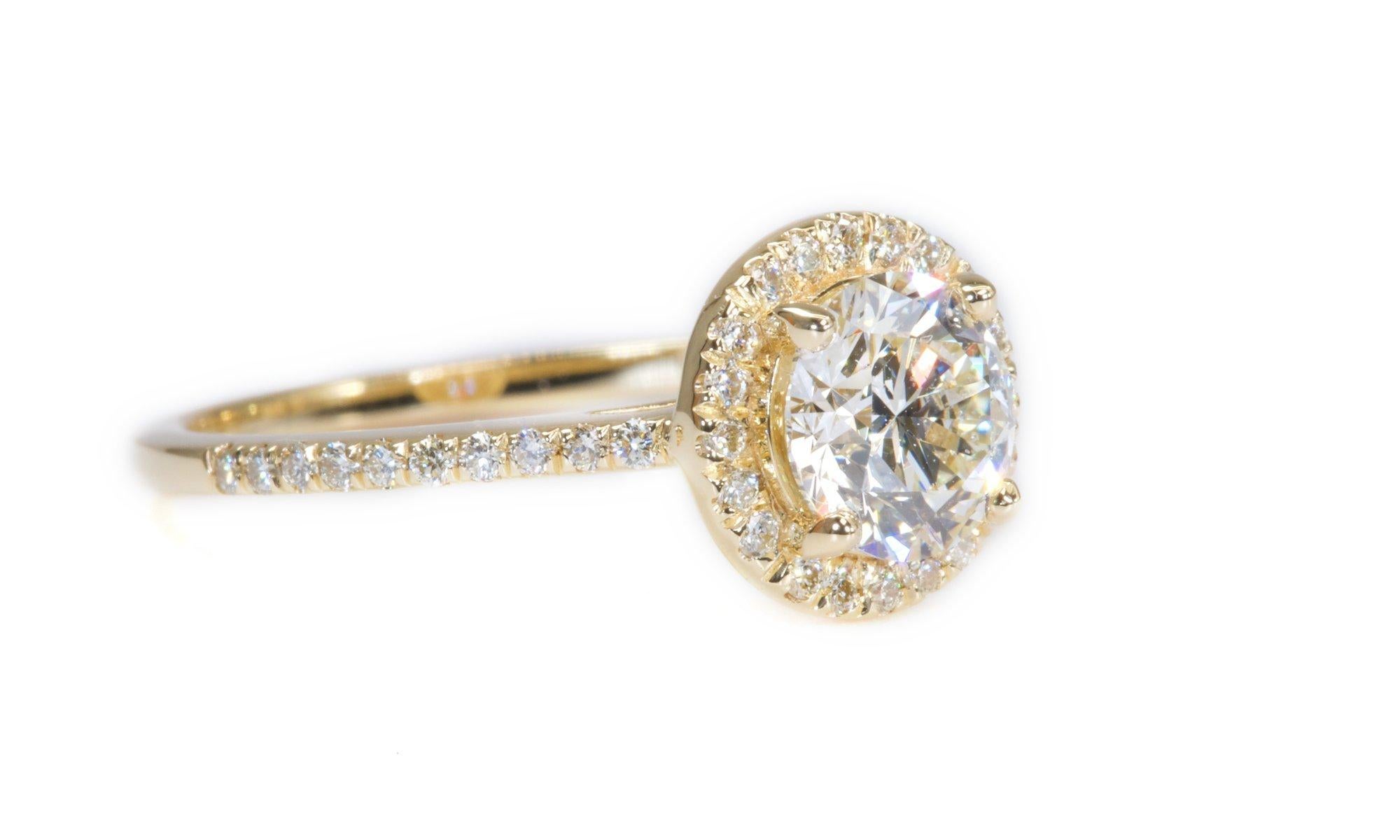 A luxurious halo solitaire ring with a dazzling 1.07 carat round brilliant natural diamond in H VS2 ideal cut. The jewelry is made of 18K yellow gold with a high quality polish. The main stone is engraved with a laser inscription and has a GIA