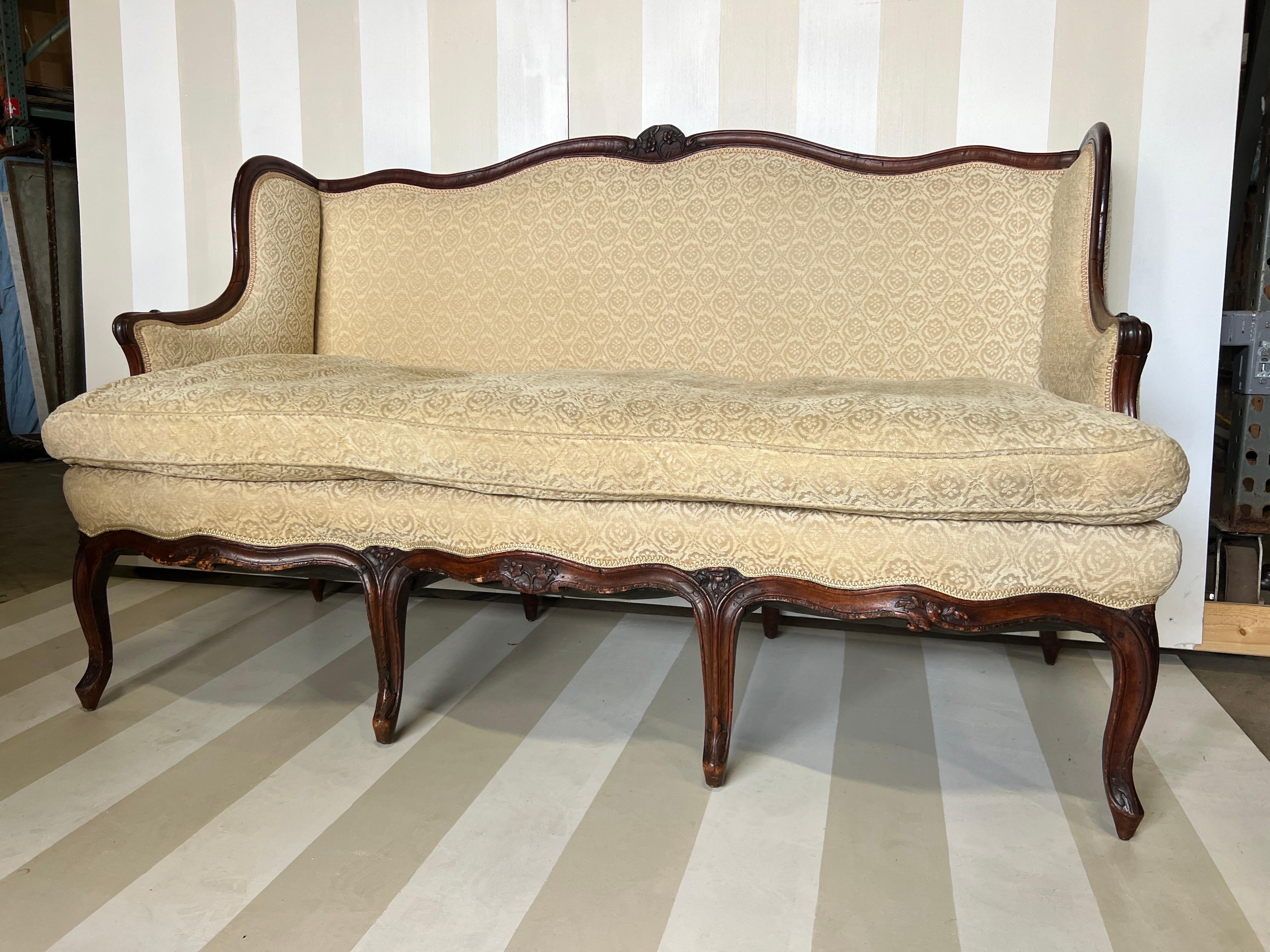 Splendido divano o divano in noce intagliato francese del XVIII secolo con motivi floreali intagliati e schienale a pannelli. Un esempio molto raffinato. Recentemente è stata tappezzata in Fortuny con un cuscino molto confortevole. 