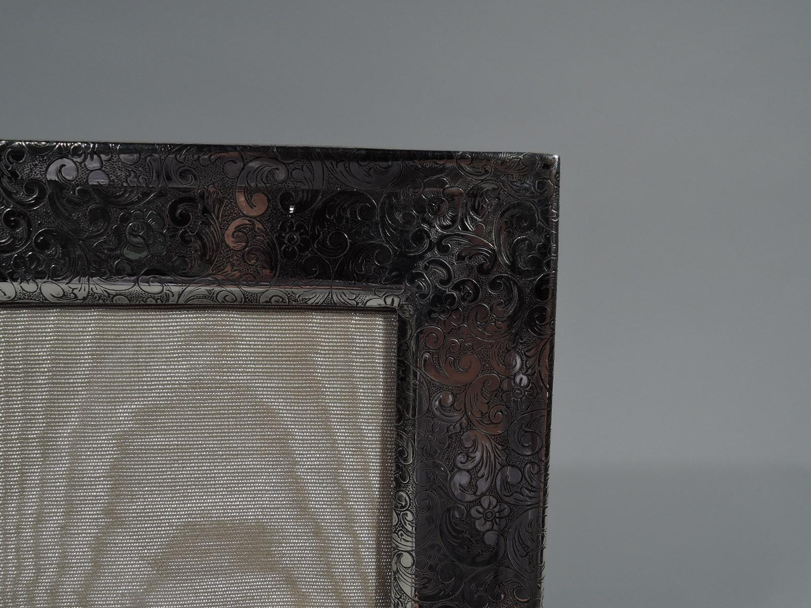 Gorgeous Art Nouveau sterling silver picture frame. Rectangular window and flat surround with beveled rims and dense, slightly hallucinatory acid-etched scrolls and flowers. With glass, silk lining, and velvet back and hinged support for portrait