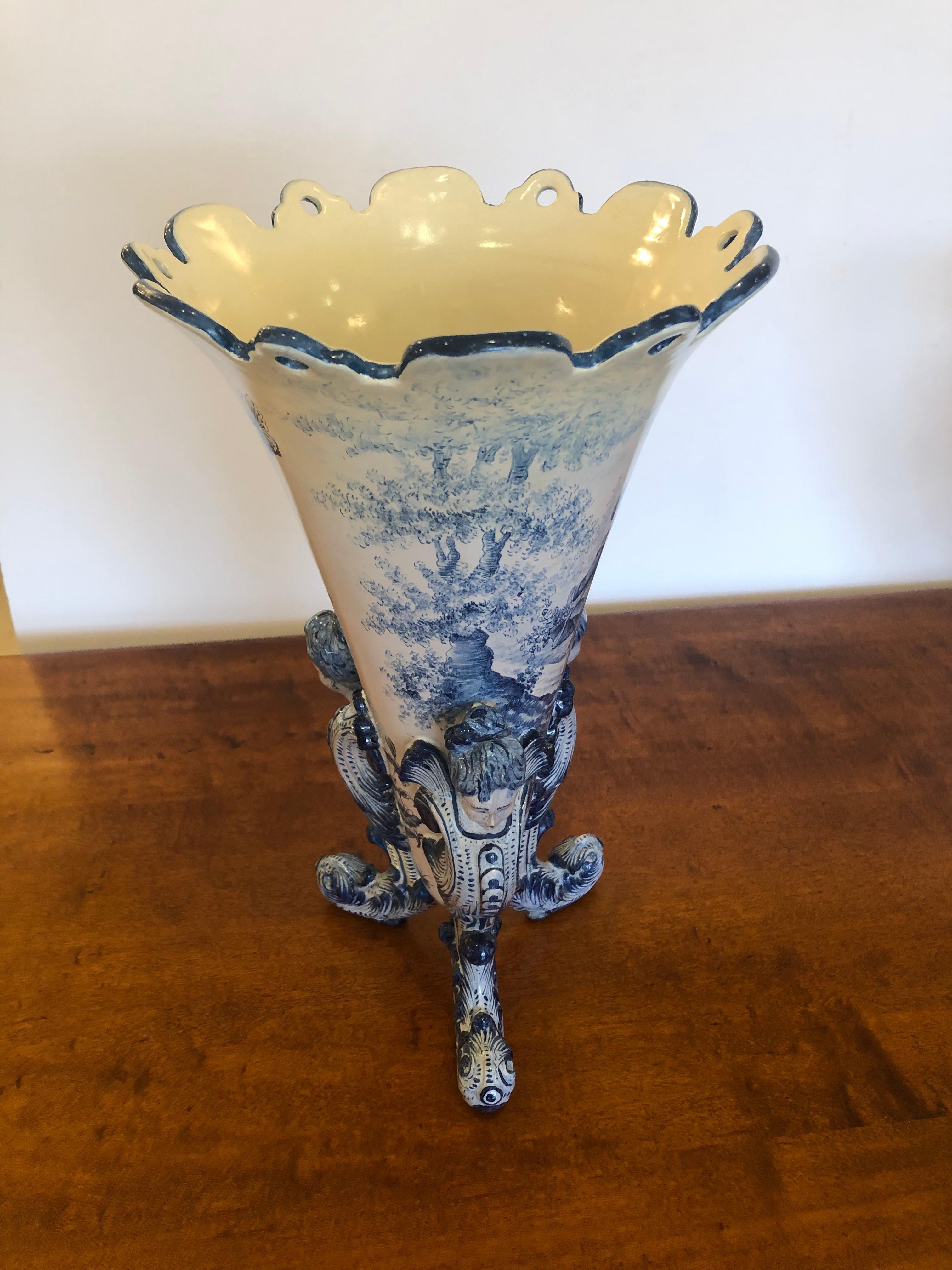 Impressive large and beautifully made Italian ceramic vase having blue and white meticulous painting of figures and landscape with tripod base made of 3 enchanting figurehead women. The top is delightfully scalloped.