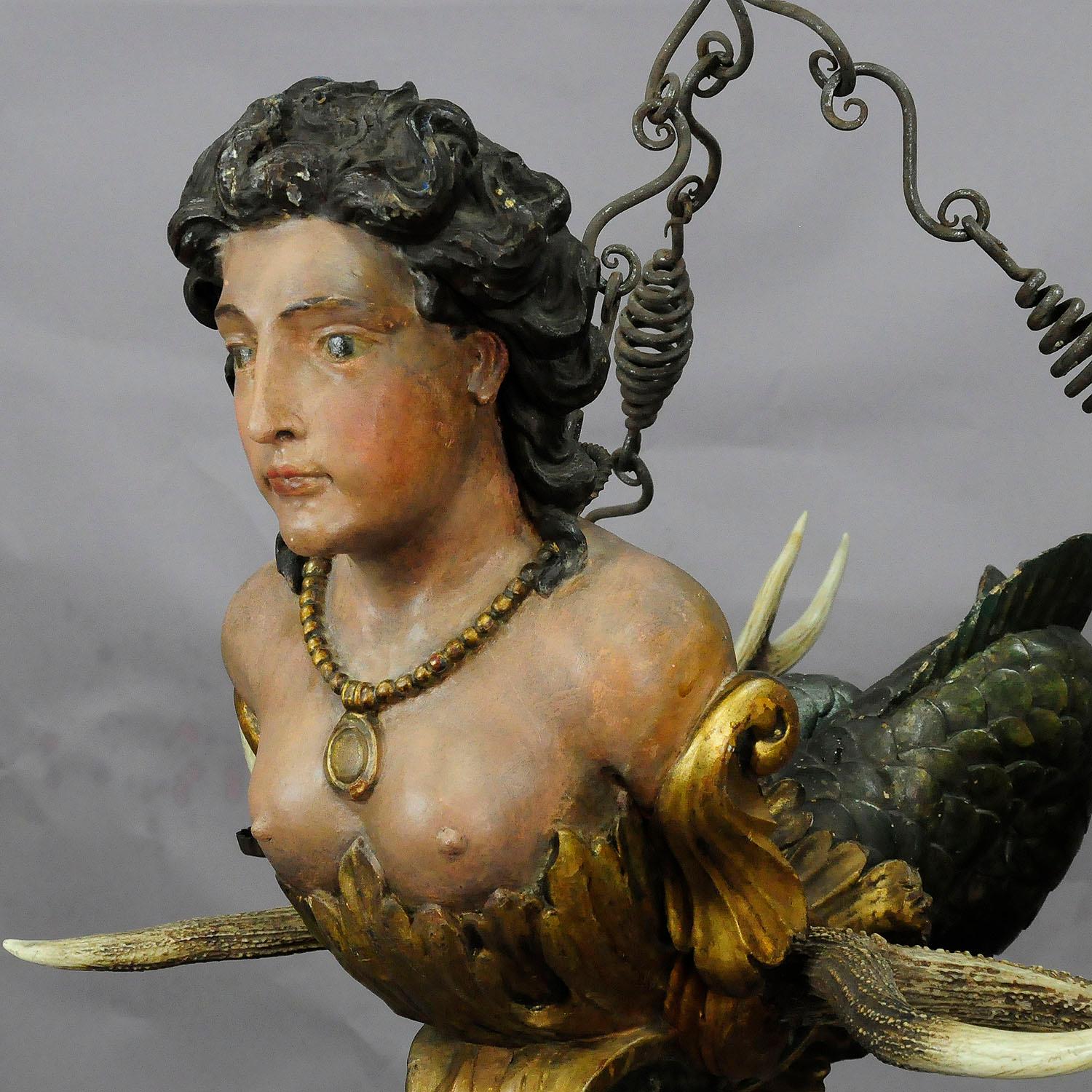 A wonderful antique 18th century lüsterweibchen. An elaborate carved and large mermaid statue attached to an impressive pair of stag antlers. Four hand forged iron spouts for candles and a hand forged suspension complete this fantastic piece. An