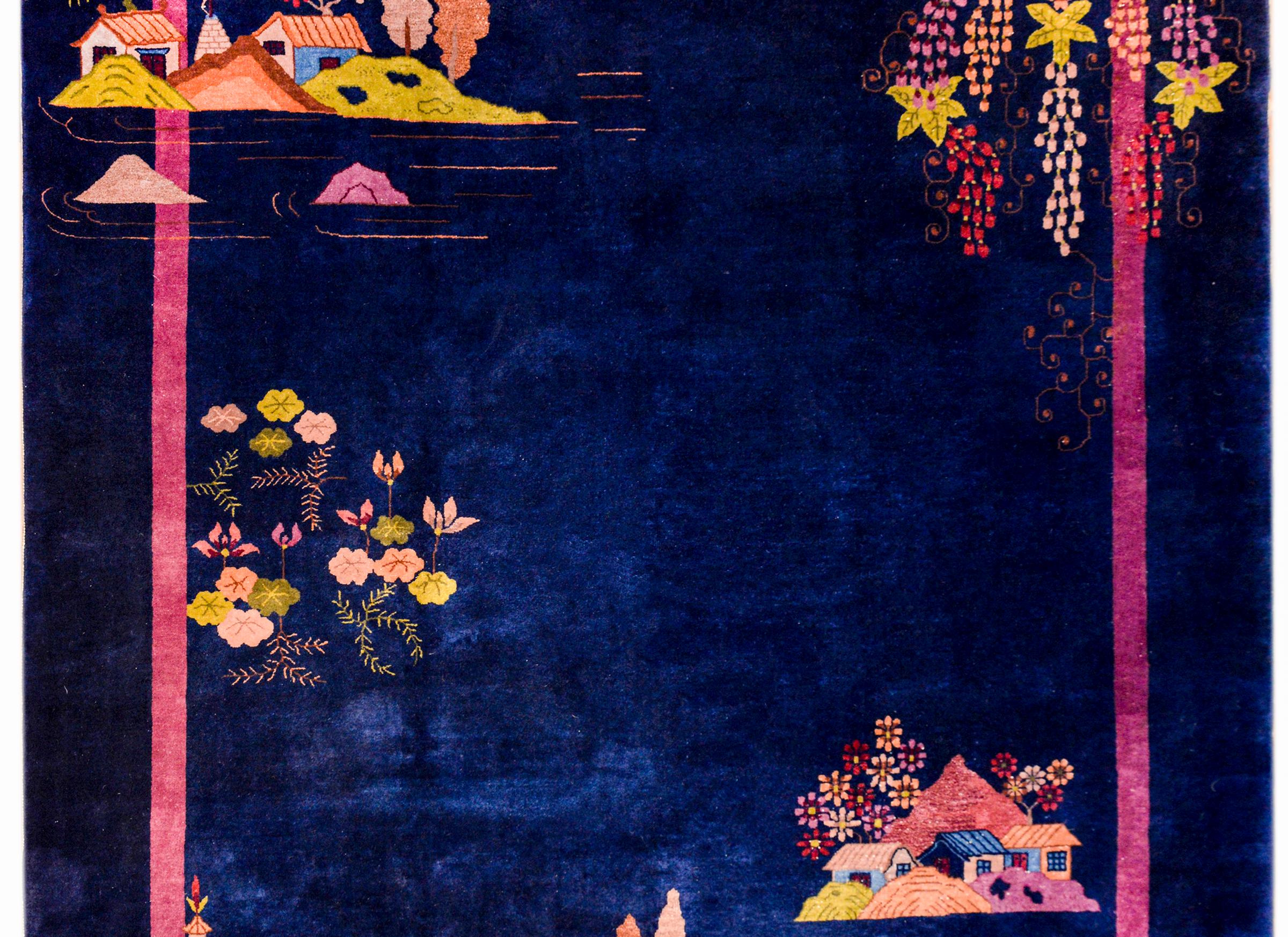 A gorgeous early 20th century Chinese Art Deco rug with an incredible dark indigo background with a thin bright pink stripe border. Three mounds with multi-colored village scenes are dotted throughout, with two cascading florals with myriad