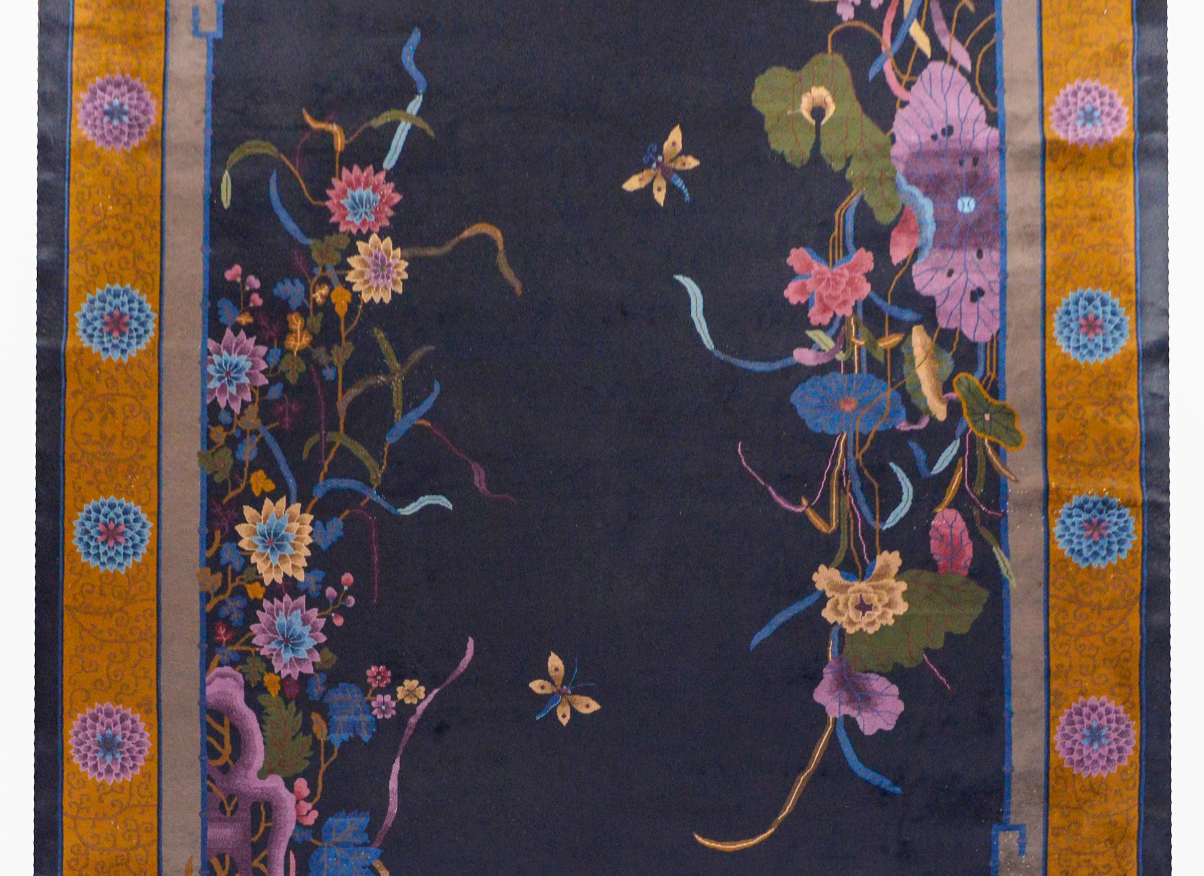 A gorgeous early 20th century Chinese Art Deco rug with large clusters of multicolored lotus and chrysanthemums in each corner on dark indigo background. The border is exciting with a wide gold stripe with a scrolling vine pattern and large round
