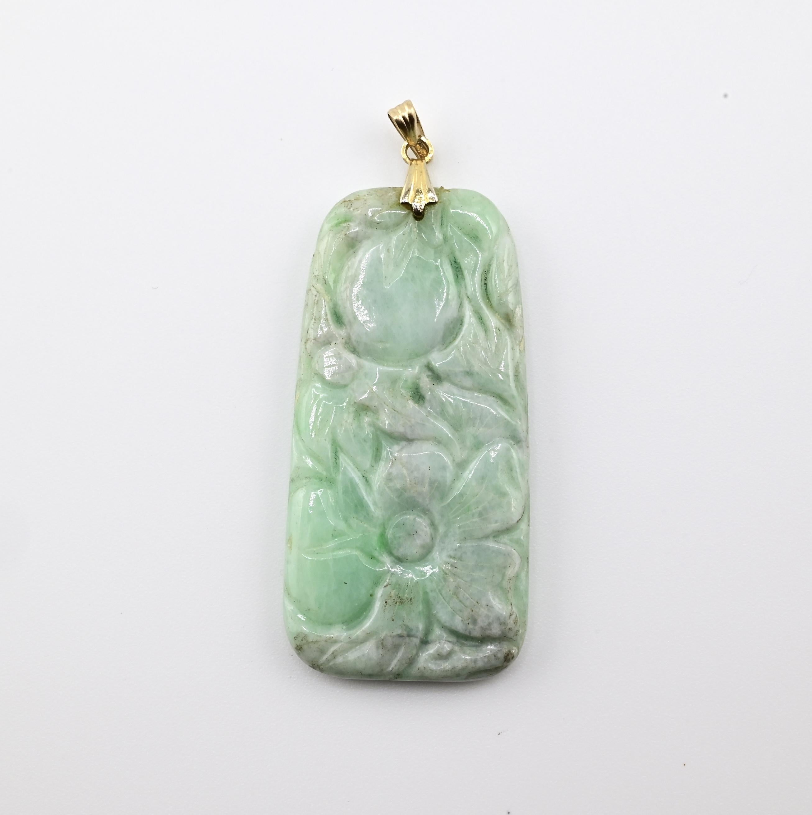 Il s'agit d'un pendentif en jade magnifiquement sculpté d'un motif floral. Le pendentif présente des détails complexes, avec un motif de fleurs et de feuilles. Le jade est d'un vert tendre avec des variations naturelles, ce qui lui donne de la