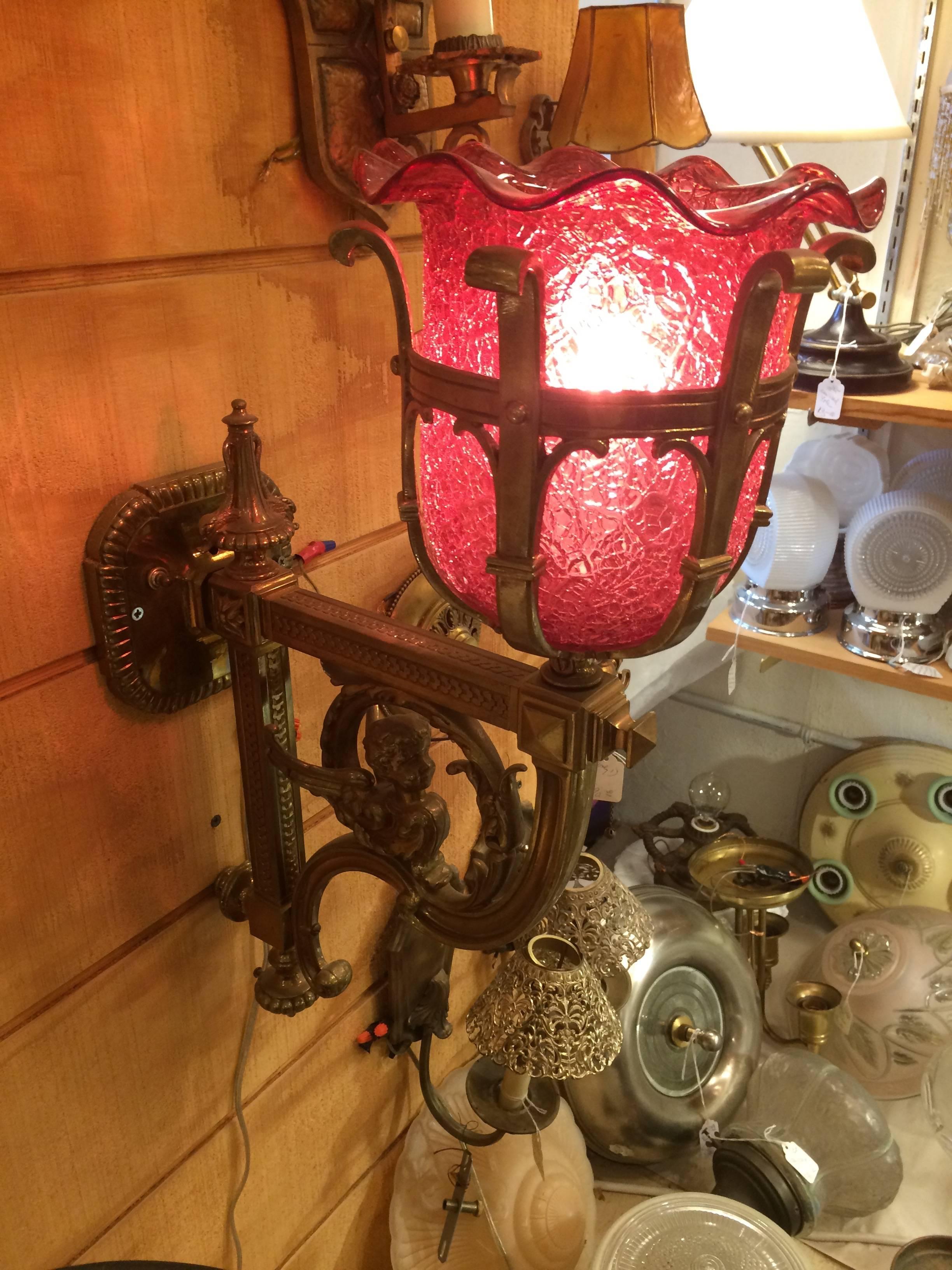 A magical antique wall sconce having elaborate brass bracket with putti and a scalloped cranberry glass shade. Rewired and ready. The brass wall mount is 15 inches high.
       