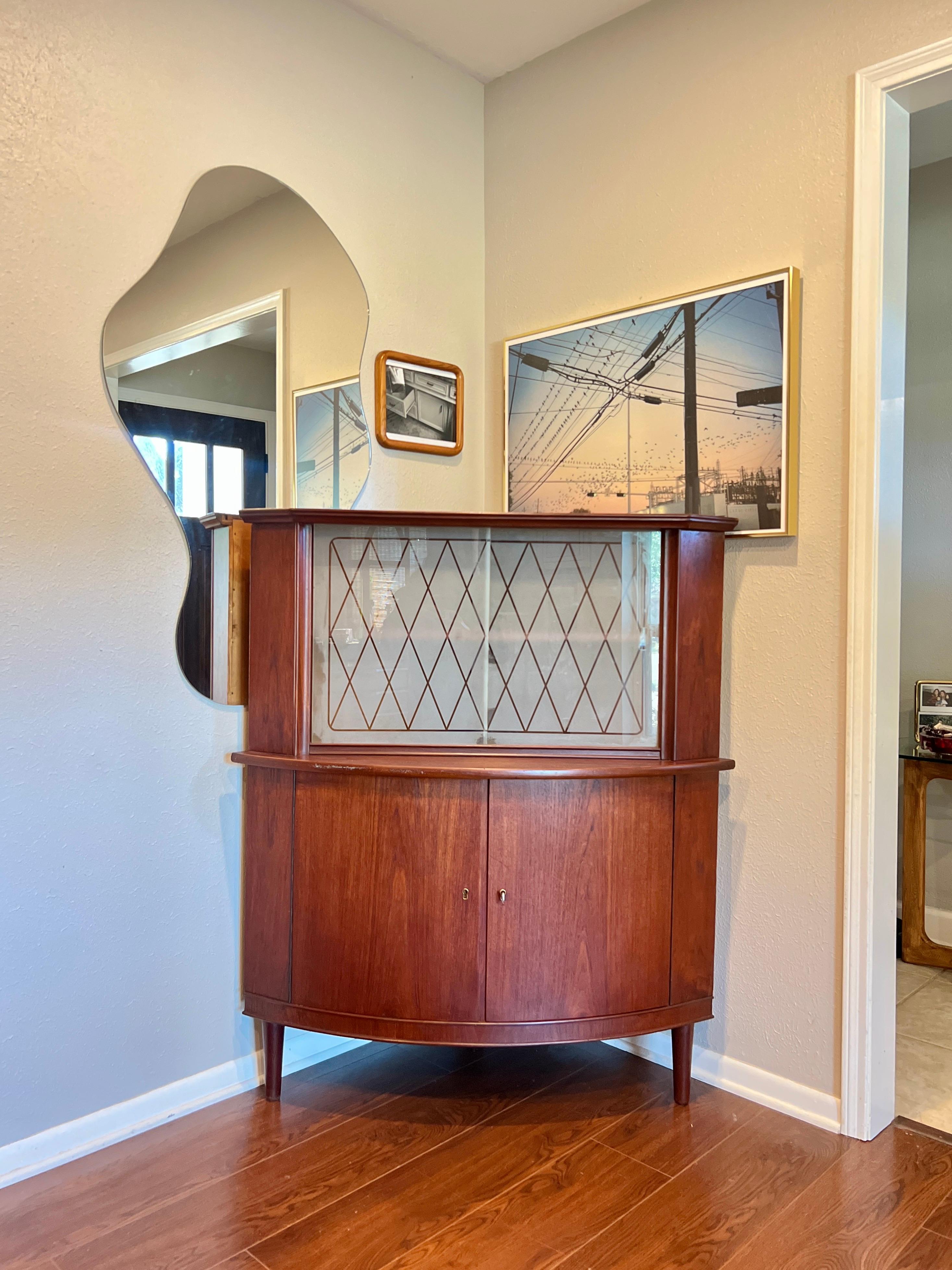 Gorgeous Danish teak corner cabinet/bar, circa 1960s. Made of solid and veneered teak with two glass doors on top and a pair of cabinet doors on the bottom. Key is included, but does not lock the cabinet. Overall in good original condition with some