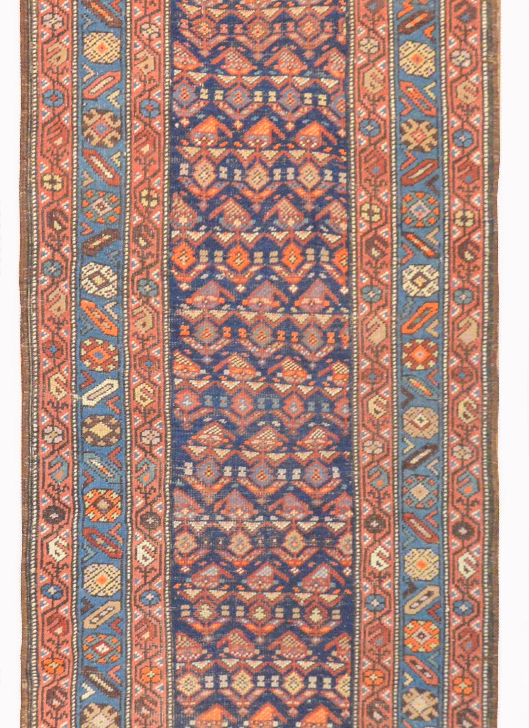 A gorgeous early 20th century Persian Azari runner with an all-over stylized paisley pattern woven in myriad colors including crimson, light and dark indigo, orange, and lavender on a dark indigo background, surrounded by three distinct stylized