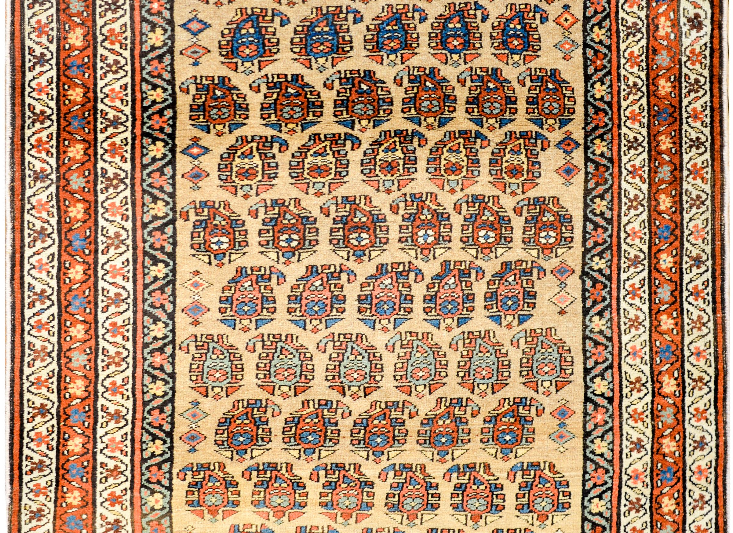 A gorgeous early 20th century Persian Bidjar rug with an all-over stylized paisley pattern woven in light and dark indigo, crimson, gold, and green, on a natural wool colored background. The border is sweet with four thin petite scrolling vine and