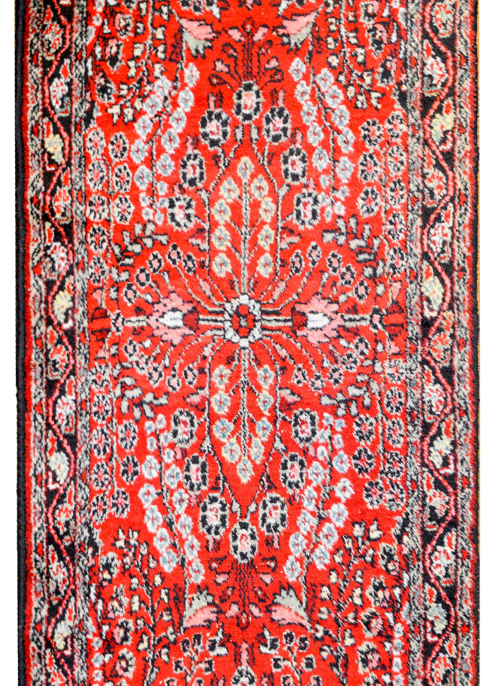A gorgeous early 20th century Persian Dargazin runner with a wonderful mirrored floral and tree-of-life pattern woven in light and dark indigo, cream, green, and gold vegetable dyed wool on a brilliant crimson background, surrounded by several