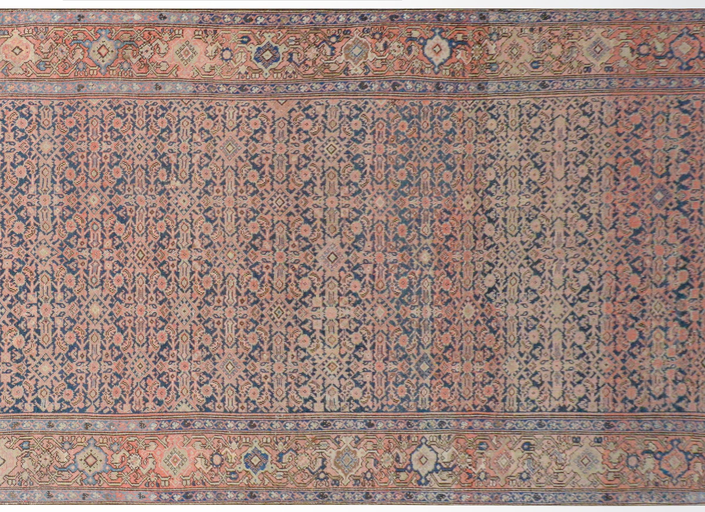 A gorgeous early 20th century Persian Herati rug with a wonderful all-over trellis floral pattern woven in pink, light indigo, and gold, on a dark indigo background surrounded by a wide border with a large-scale floral and scrolling vine pattern.