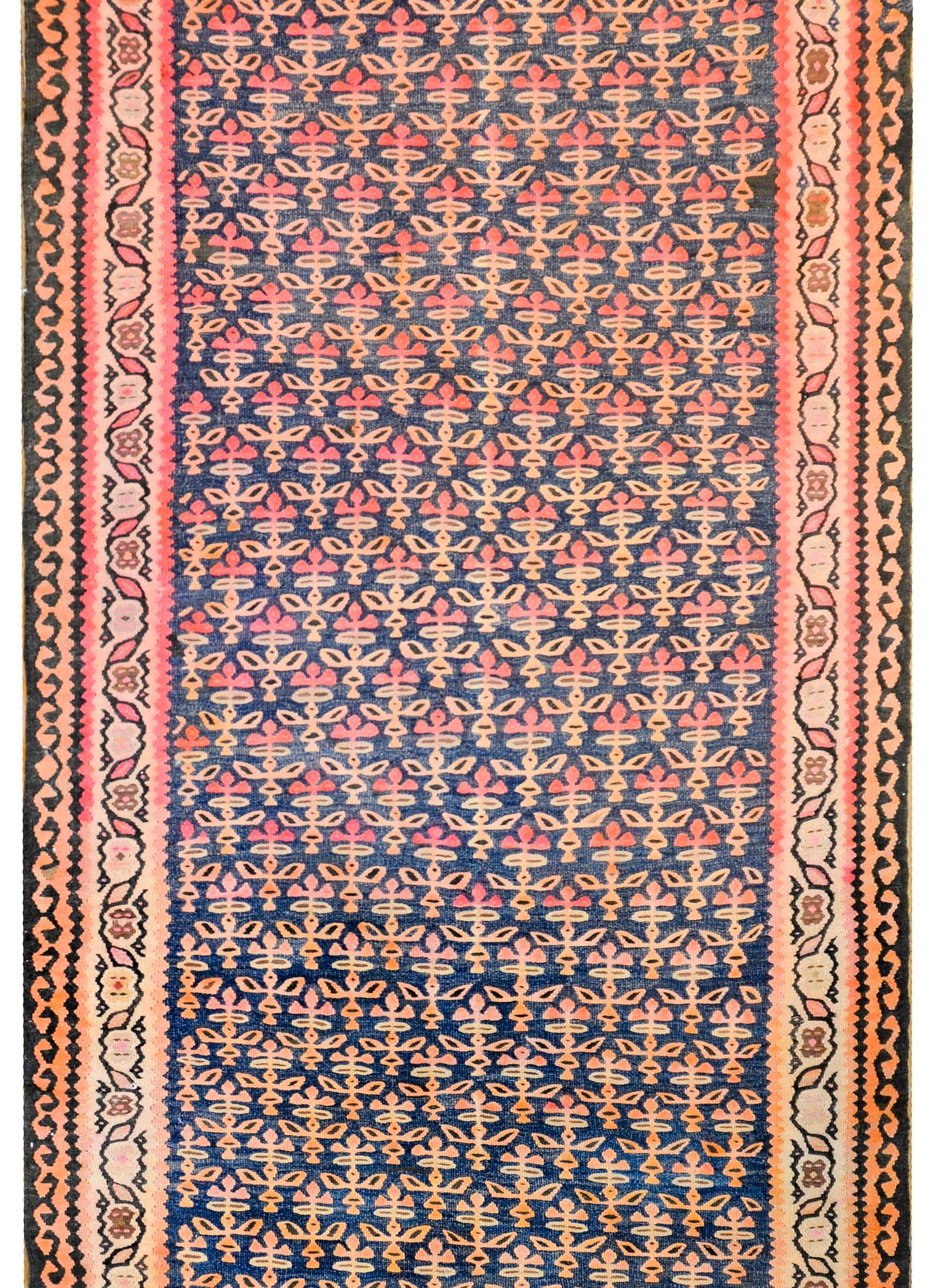 A gorgeous early 20th century Kurdish kilim rug with a beautiful petite tree-of-life pattern woven in gold and crimson, on a dark indigo background. The border is wonderful, with a petite leaf and vine pattern on the inside, and a stylized leaf