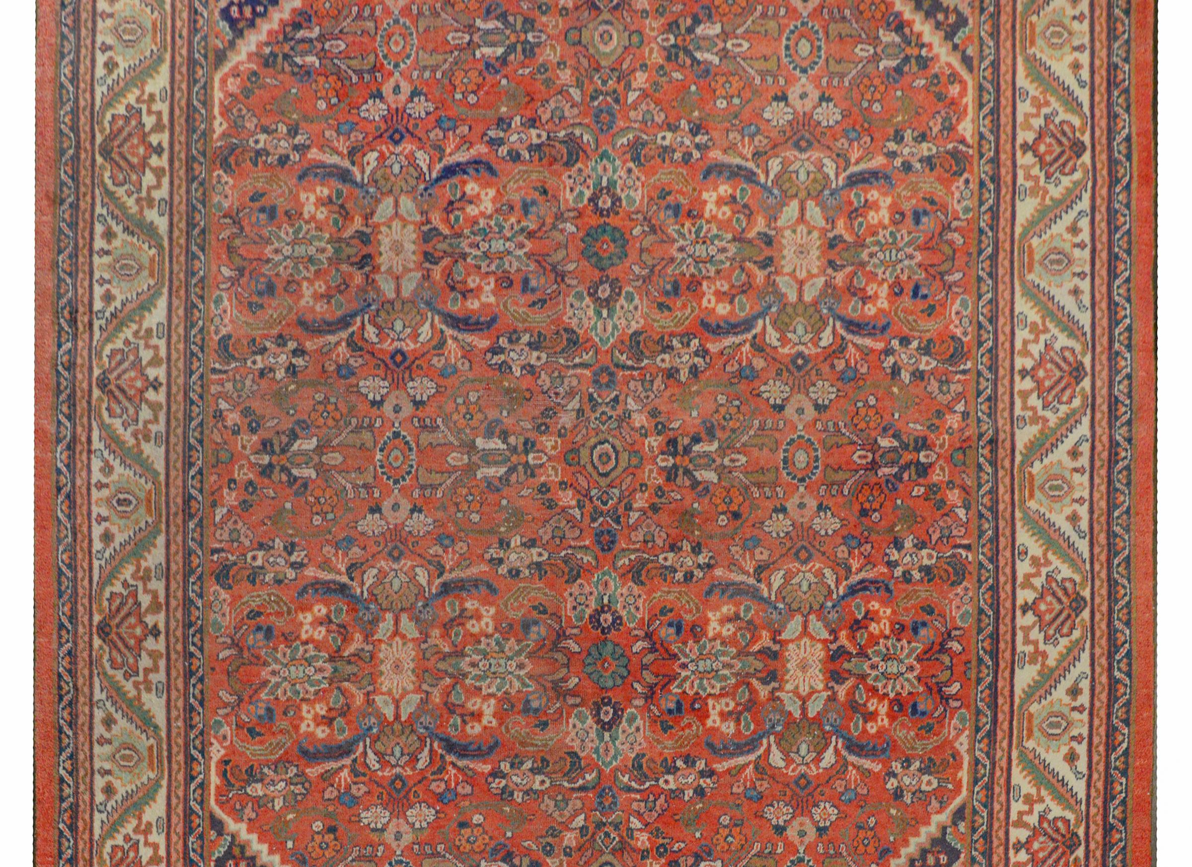 A gorgeous early 20th century Persian Mahal rug with a mirrored pattern containing four large floral medallions amidst a field of flowers, all woven in light and dark indigo, cream, green, and brown in a crimson background. The border contains a