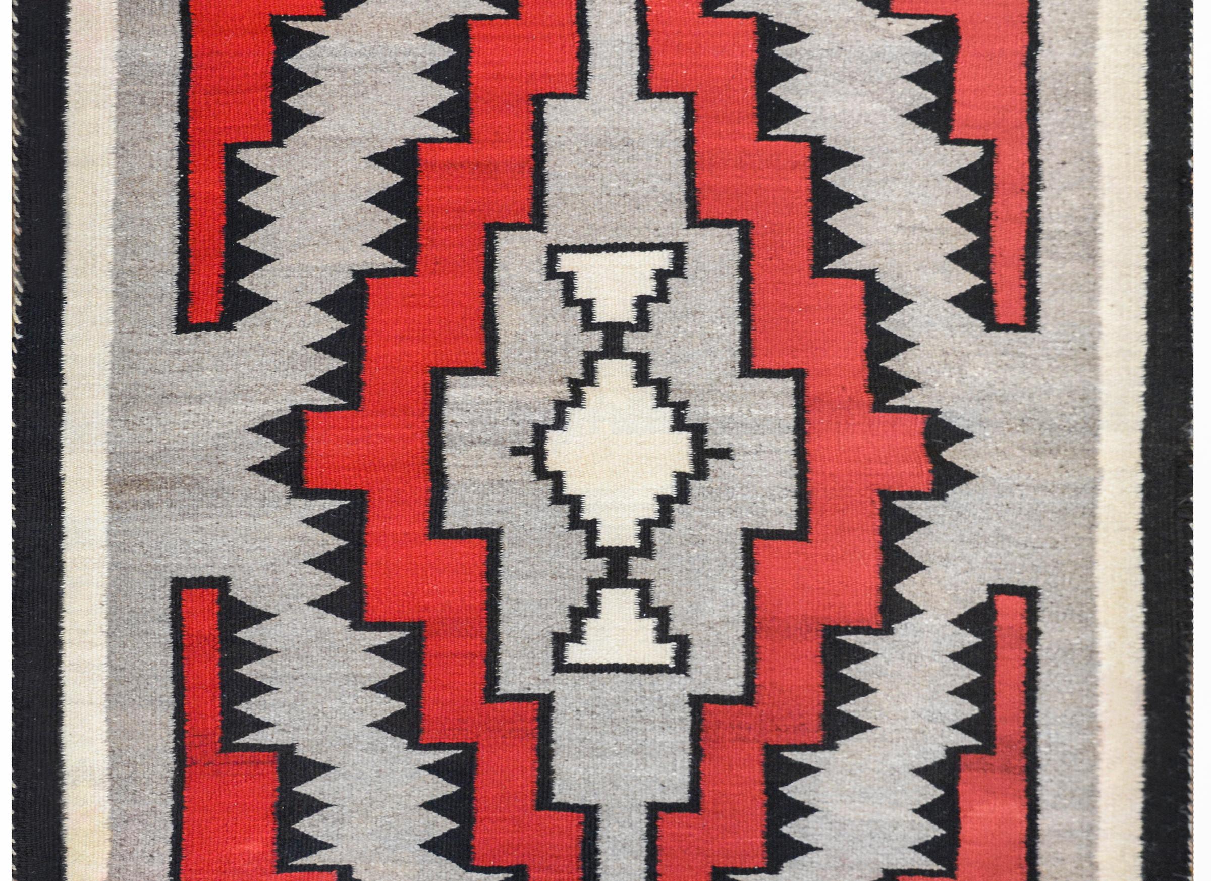 A gorgeous early 20th century Navajo rug with a fantastic pattern containing stepped crimson and gray diamonds trimmed with black triangles, all on a gray background. The border is simple with solid black and cream colored stripes.