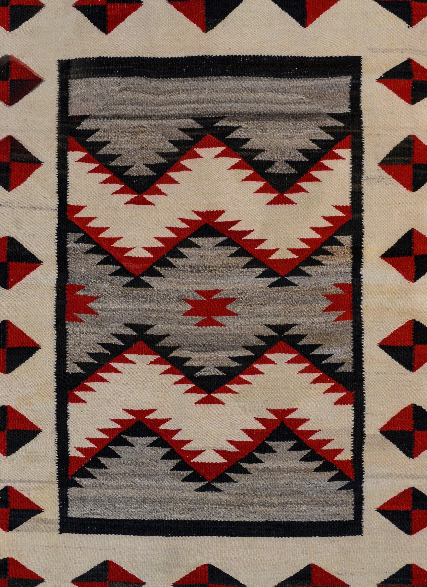 A gorgeous early 20th century Navajo rug with a fantastic pattern containing a zigzag pattern field woven in crimson, black and white wool on a gray background. The border is wonderful with a wide central white stripe with a repeated pattern of