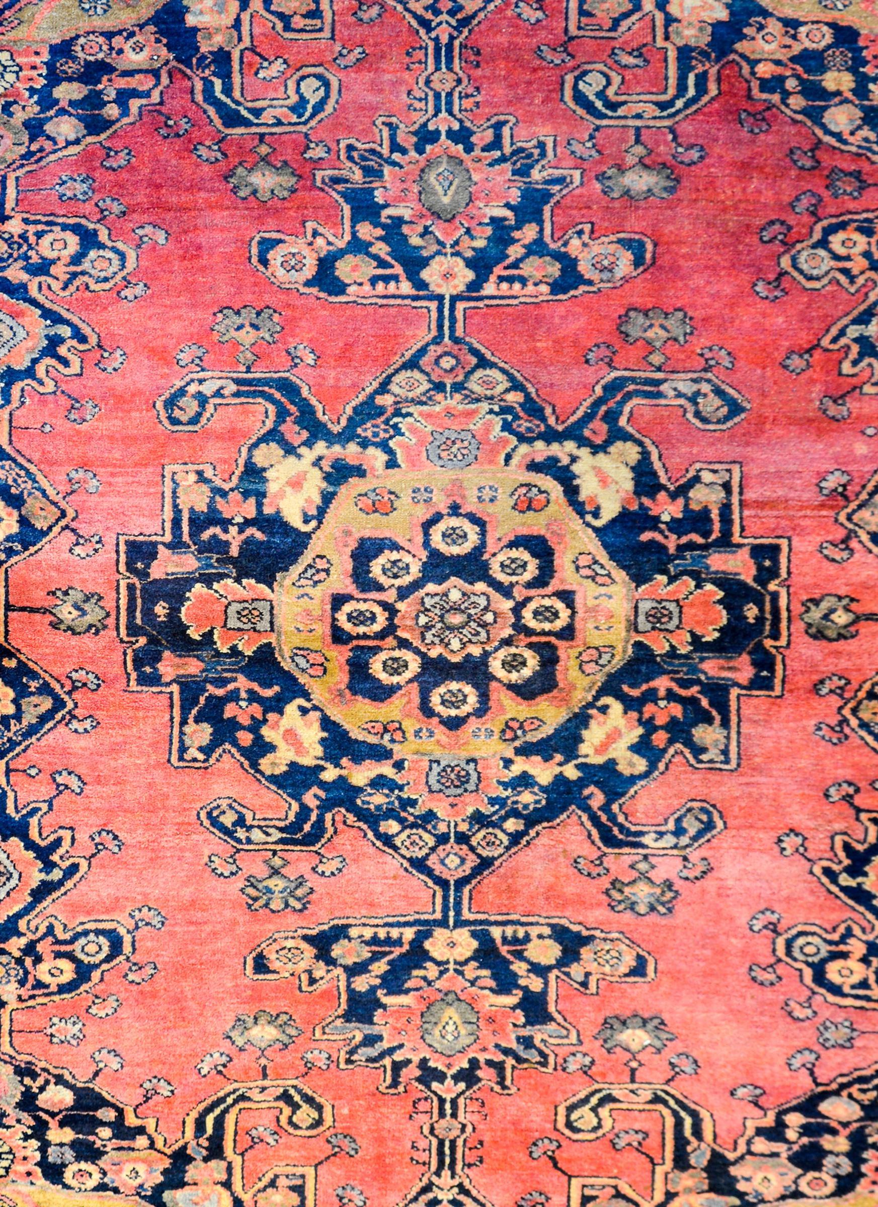 A gorgeous early 20th century Persian Nehevand rug with a large-scale bold tribal pattern containing a large medallion with stylized flowers woven in gold, salmon, indigo, and cream colored wool on a beautiful abrash salmon ground. The border is