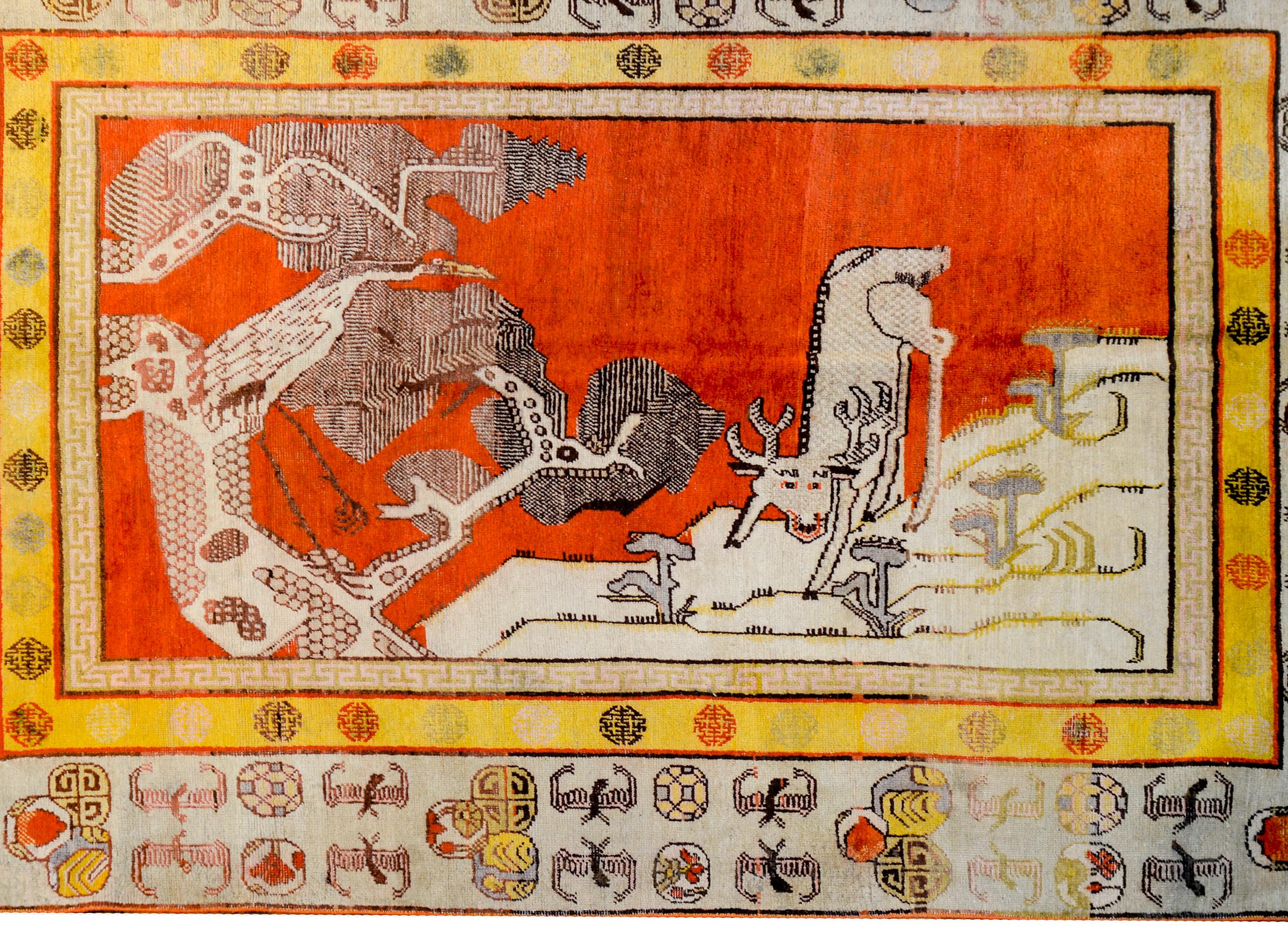Magnifique tapis Khotan pictural du début du XXe siècle en Asie centrale représentant un cerf sur une montagne avec une grue perchée dans un pin tordu sur fond de ciel orange brillant. La bordure est magnifique avec une large bande extérieure