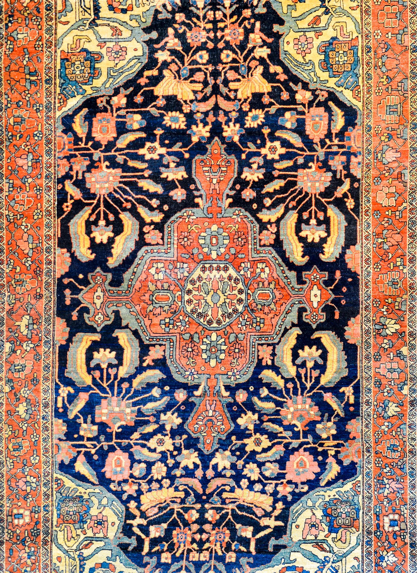 A gorgeous early 20th century Persian Sarouk Farahan rug with a fantastic large scale crimson floral medallion with myriad flowers and scrolling vines on a dark indigo background also with myriad flowers and scrolling vines. The border is wonderful