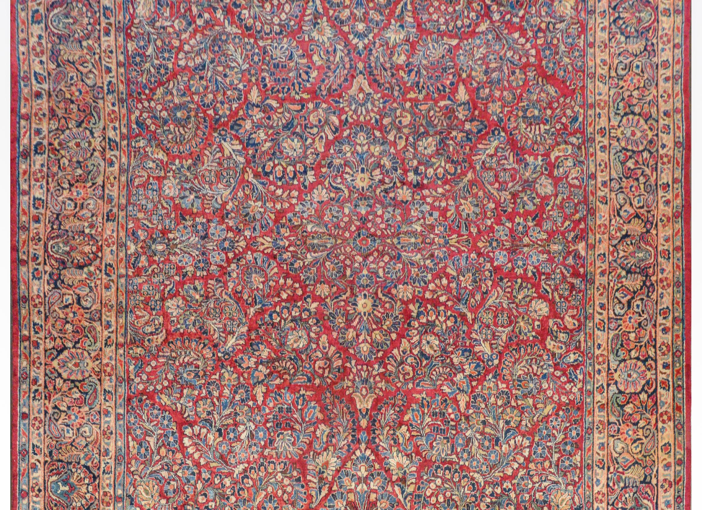A gorgeous early 20th century Sarouk rug with a fantastic pattern of clusters of myriad flowers all woven in light and dark indigo, cream, orange, and light green vegetable dyed wool on a dark cranberry background. The border is beautiful with