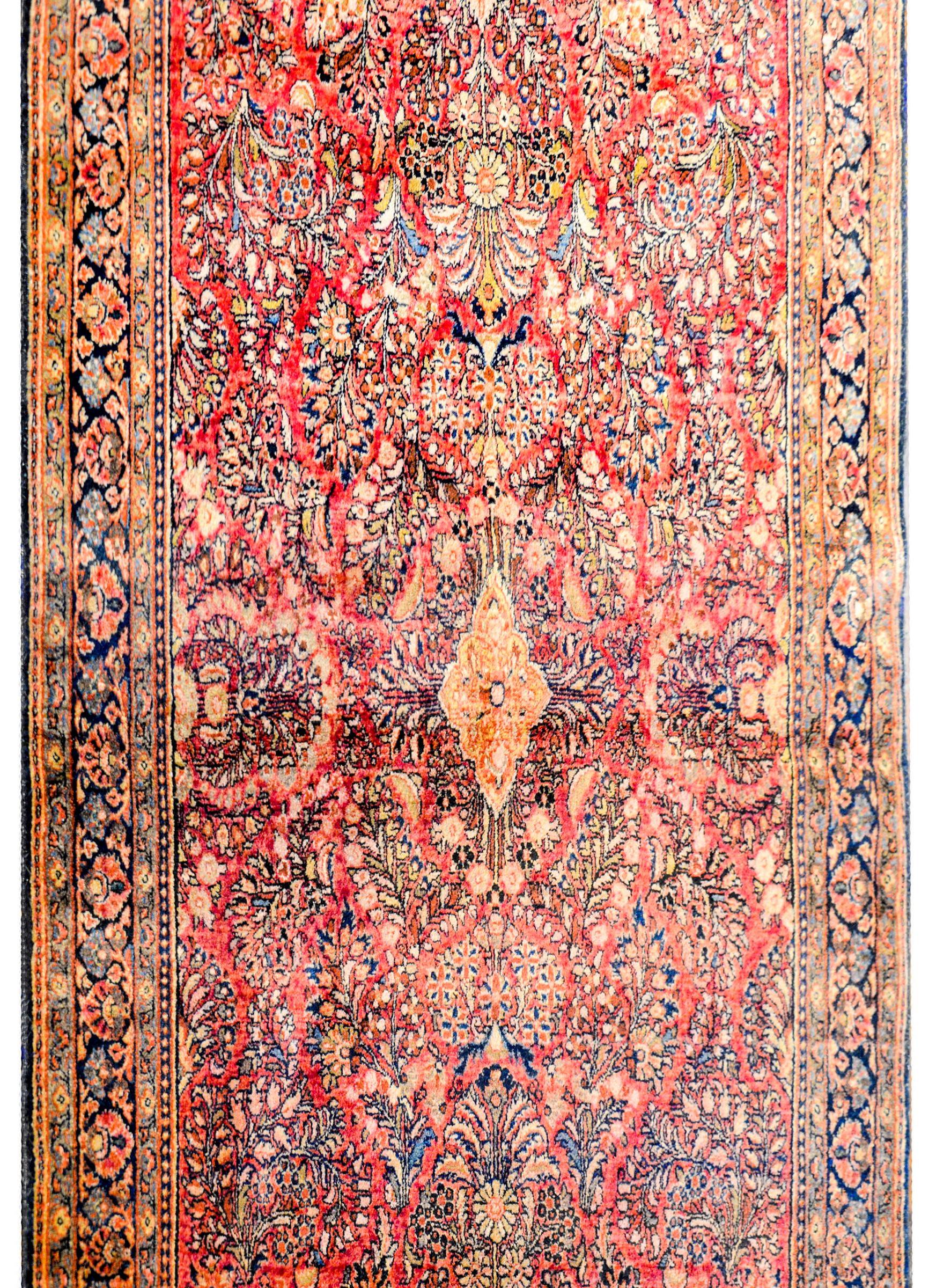 A gorgeous early 20th century Persian Sarouk rug with a wonderful central floral medallion amidst a field of myriad flowers and leaves, all woven in light and dark indigo, cream, and cranberry colored background. The border is complementary woven