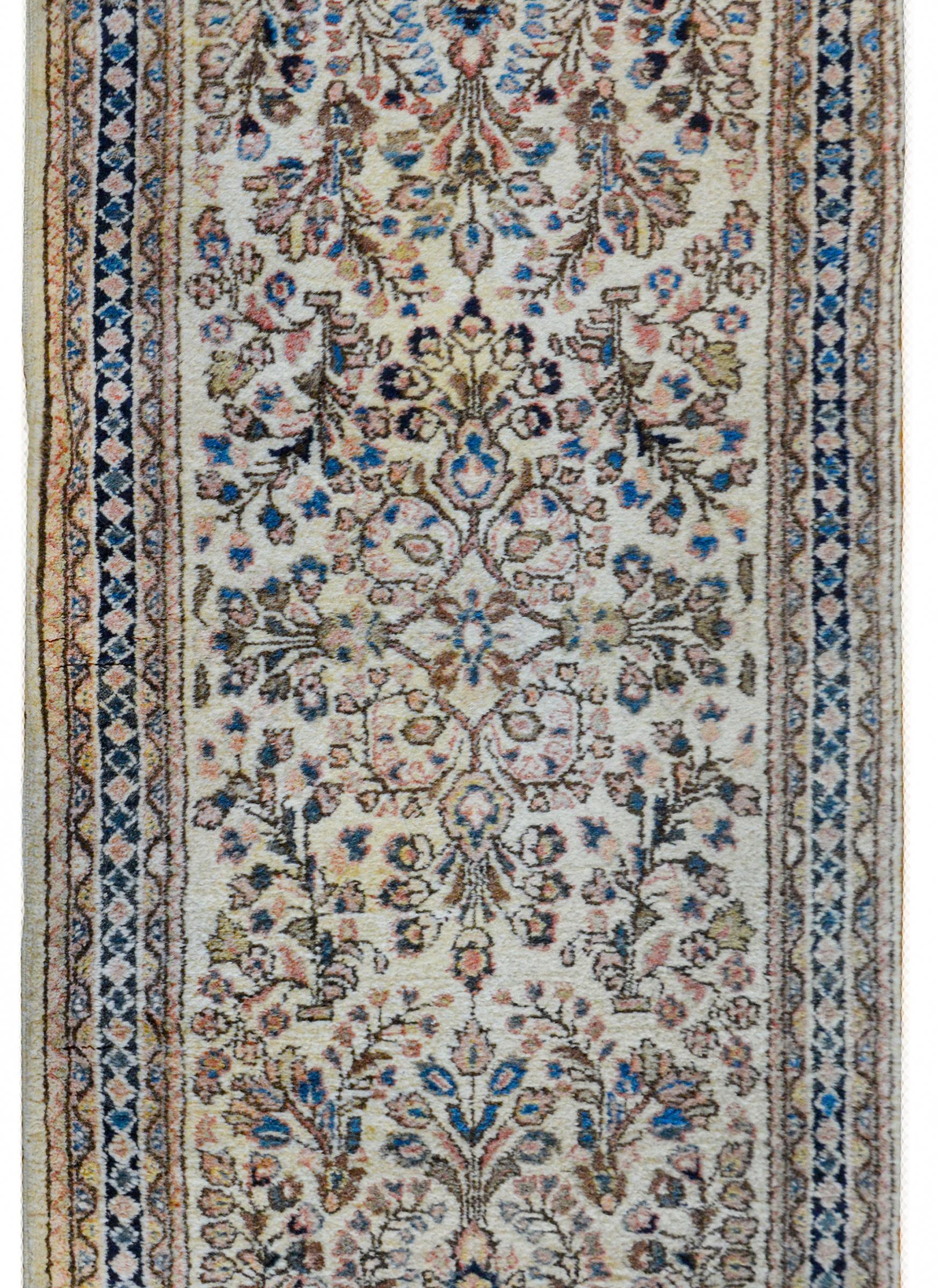 A gorgeous early 20th century Persian Sarouk rug with a wonderful mirrored floral and scrolling vine pattern woven in light and dark indigo, cream, gold, brown, and pink colored vegetable dyed wool, against a natural cream colored background. The