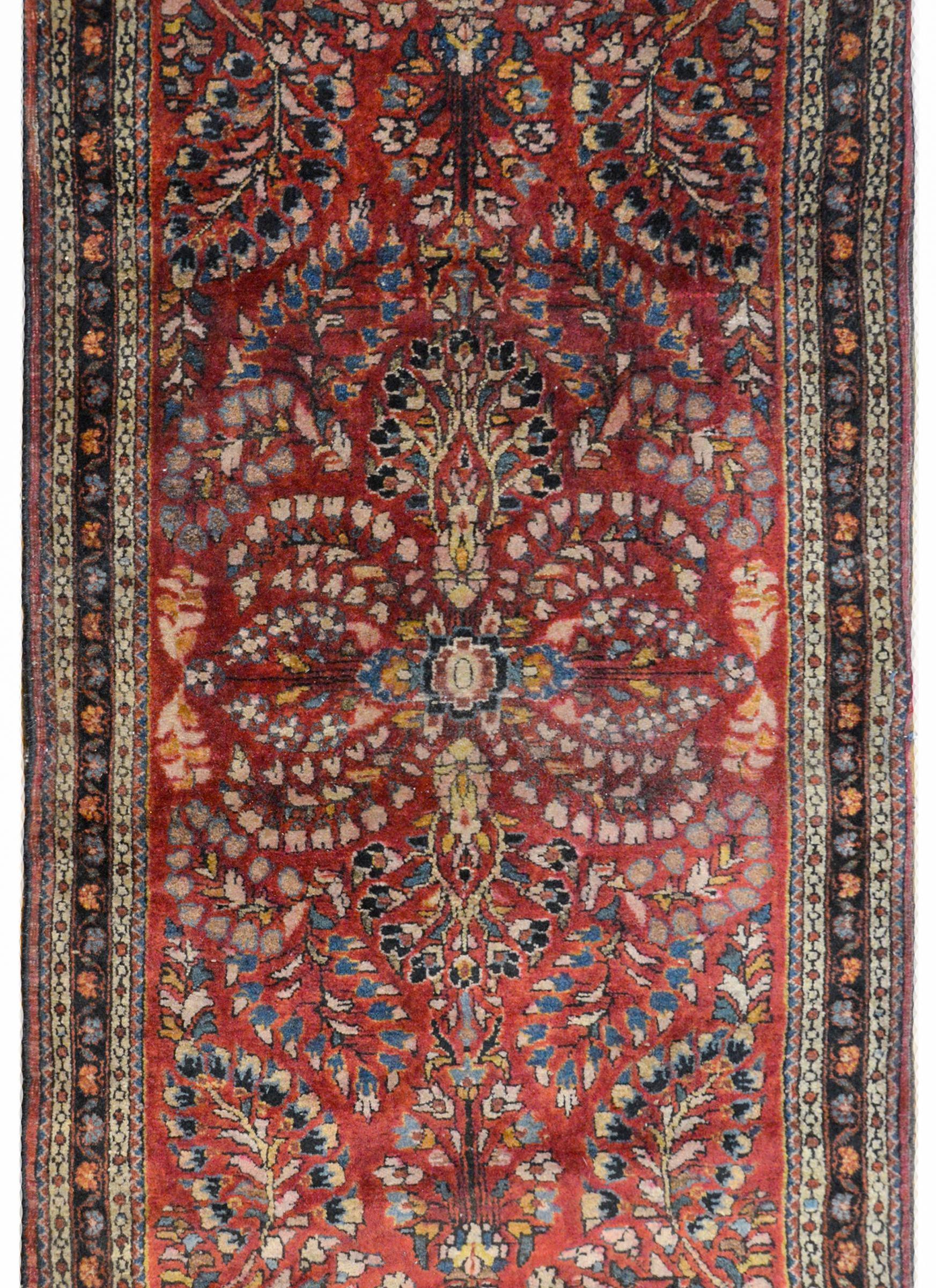 A gorgeous early 20th century Persian Sarouk rug with a wonderful mirrored floral and scrolling vine pattern woven in cream, light and dark indigo, orange, gold, and pink wool against a dark cranberry background. The border is sweet, with a wide