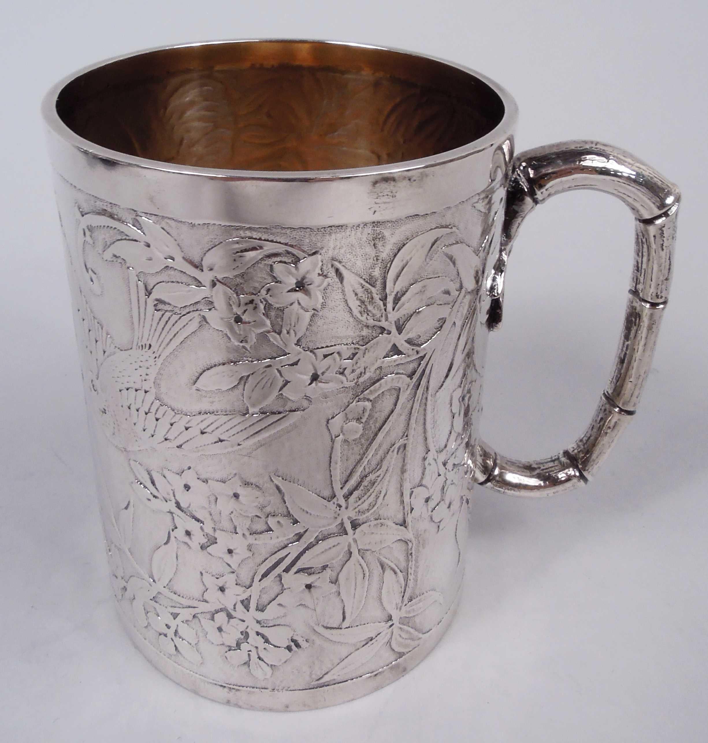 Gorgeous Victorian Japonesque sterling silver baby cup. Made by William Hunter in London in 1877. Straight and upward tapering sides; leaf-mounted bamboo-style c-scroll handle. Dense and stylized acid-etched ornament with birds flitting amongst