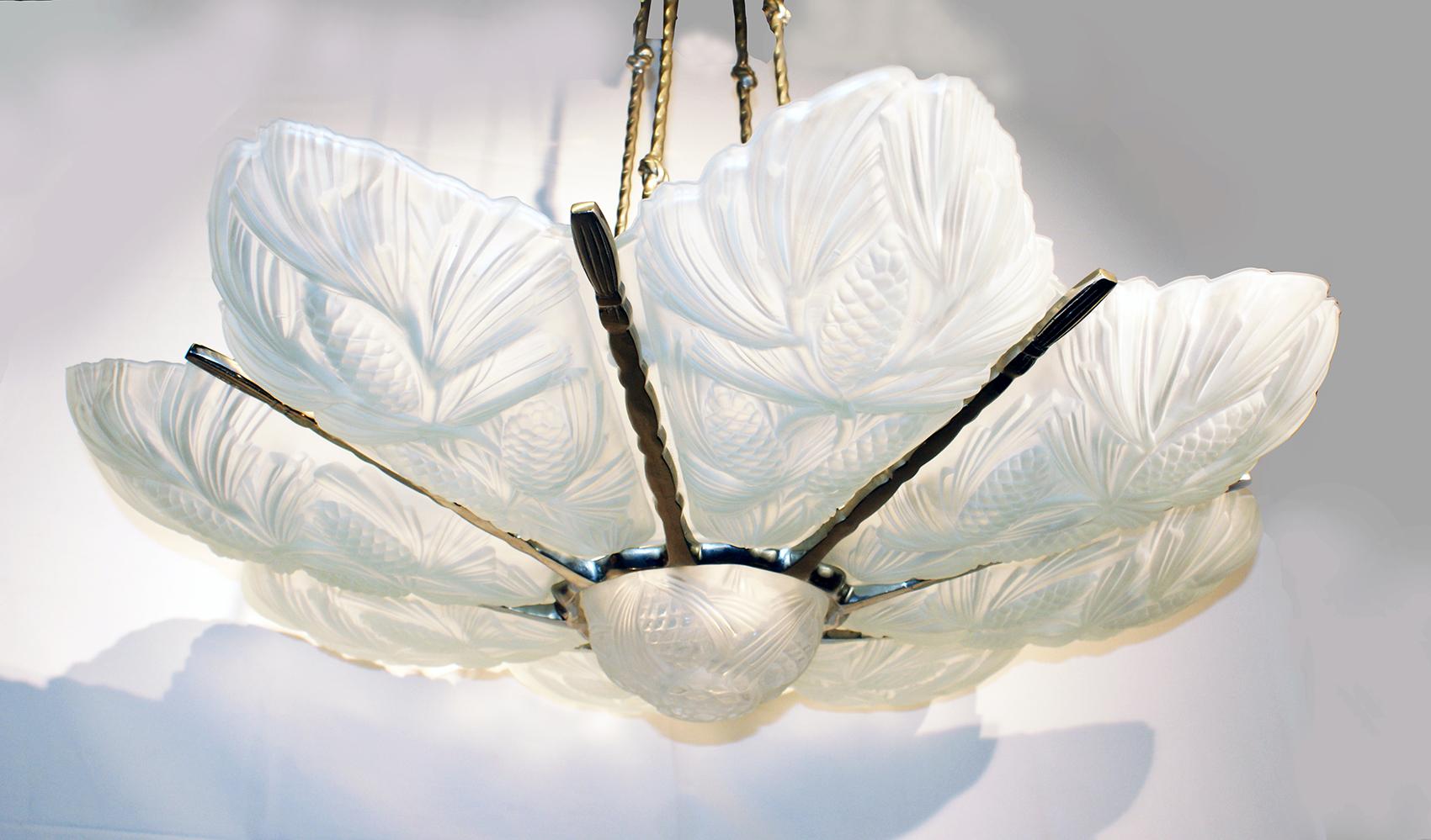 Un grand lustre Art Déco français par Marius Ernest Sabino, ayant huit panneaux en verre dépoli clair avec : un abat-jour en forme de pomme de pin qui illumine une coupe centrale en verre avec un motif floral en pin.
S'adapte à neuf ampoules