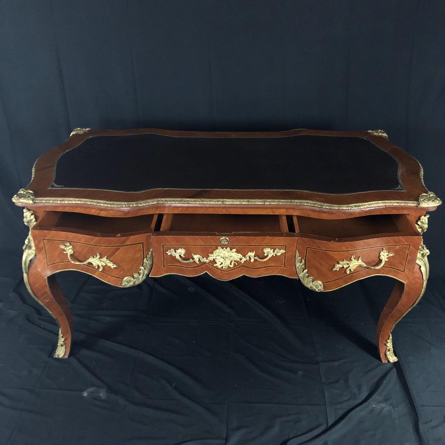 An elegant French Louis XV style walnut and ormolu gilt mounted figural bureau plat desk having rectangular top inset with a gilt tooled black leather writing panel, fitted with three apron drawers, raised on tapered cabriolet legs headed by finely