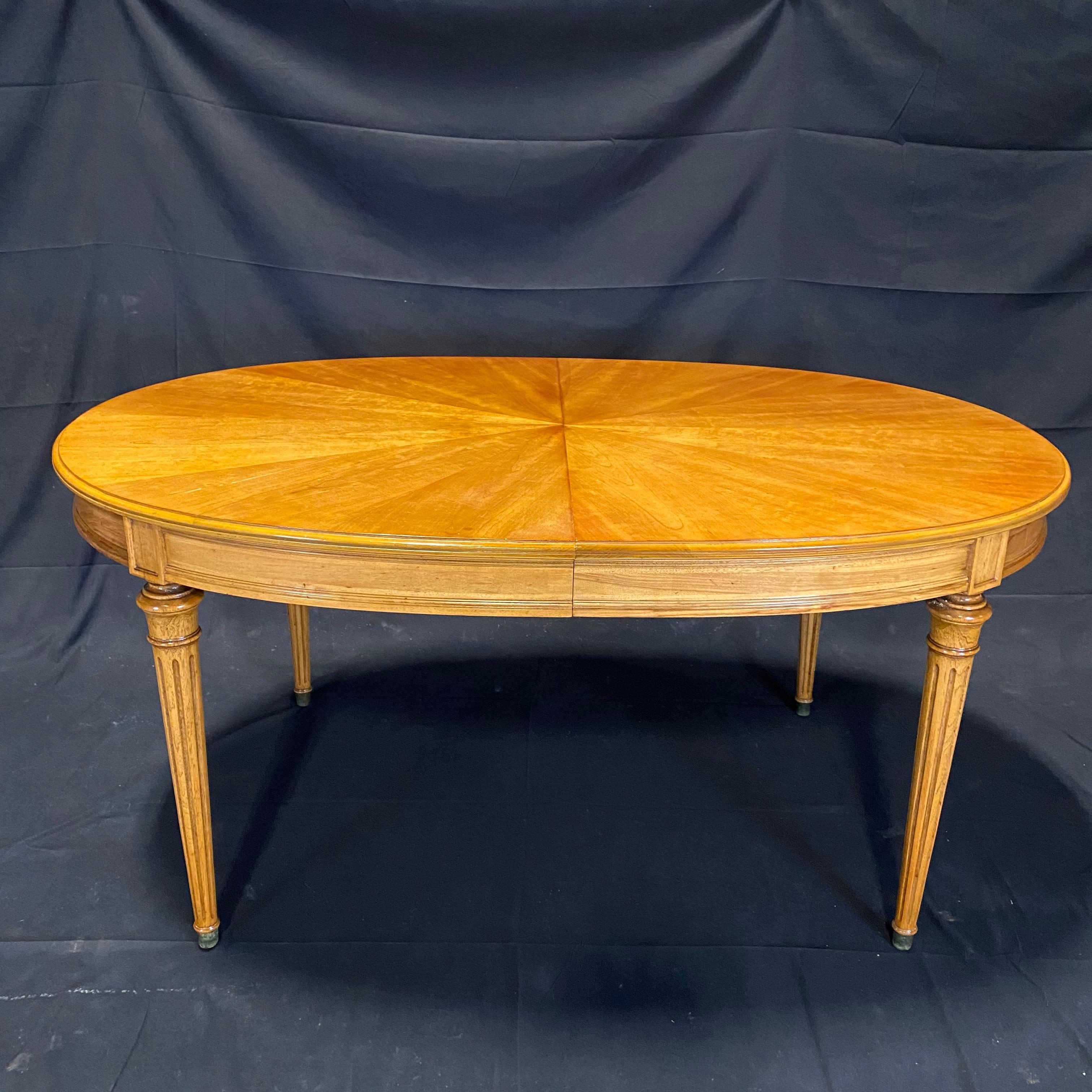A beautiful Louis XVI style French dining table with sunburst top having a well proportioned oval design that comfortably seats six without the leaves and eight with 2 leaves. The table features a beautiful sunburst veneer to the top and a carved