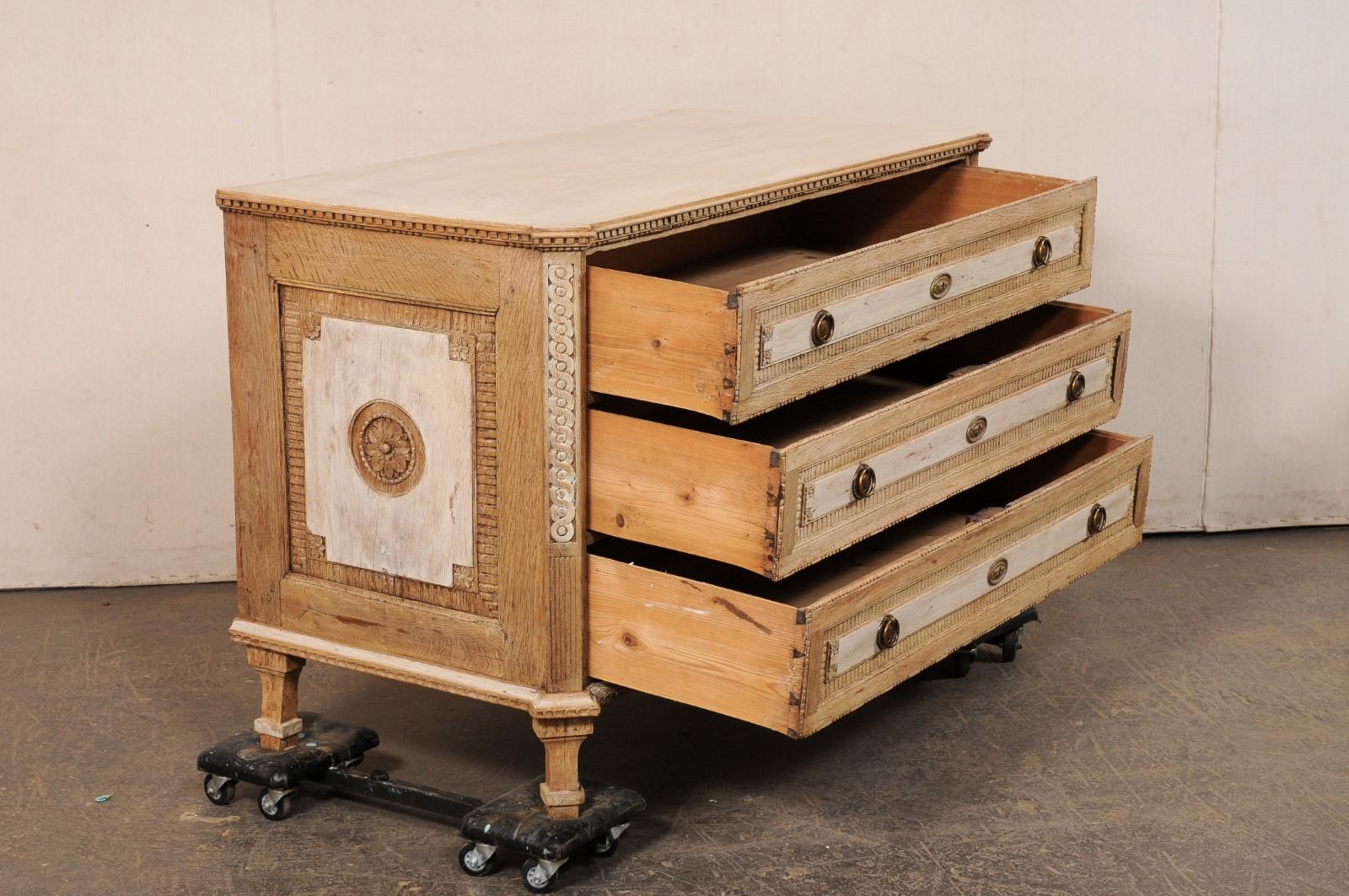 Cassettone a tre cassetti in stile neoclassico francese, intagliato e sbiancato in modo unico, risalente alla metà del XIX secolo. Questa antica cassapanca francese presenta un piano di forma rettangolare con angoli anteriori inclinati, che poggia