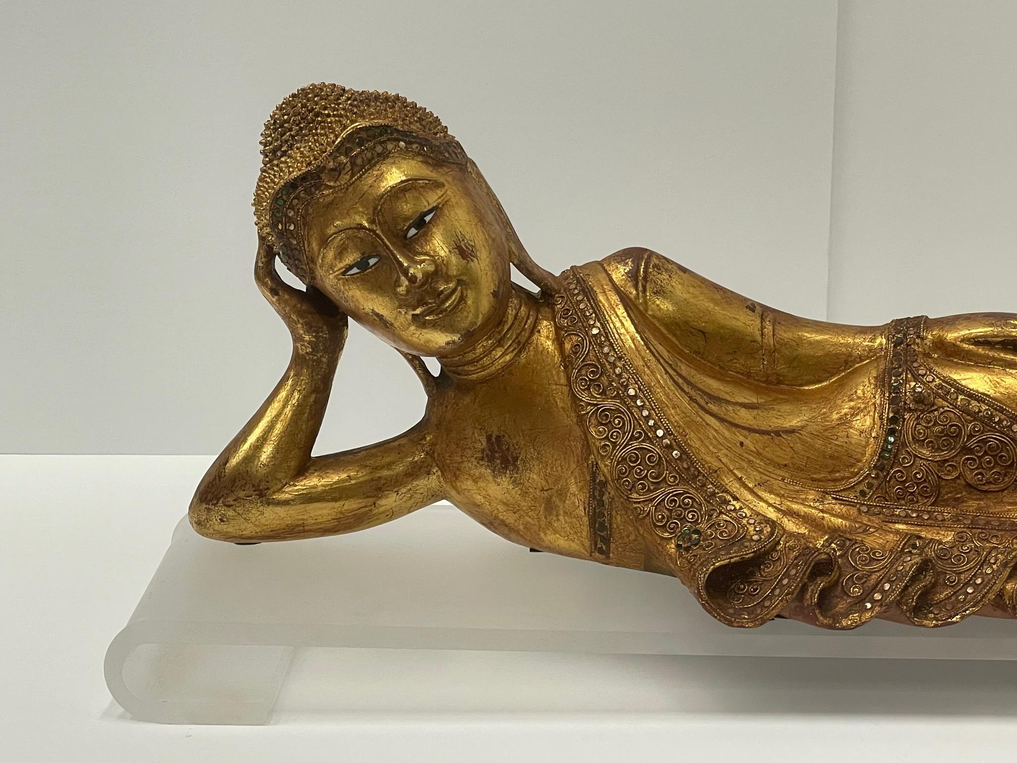 An unusual and striking giltwood sculpture of a reclining Buddha with head on one bent arm, lovely from every angle. Small glass beads are a decorative embellishment. A custom frosted lucite stand comes with the art.
Base is 32 L 8 D 2 H
Buddha 29