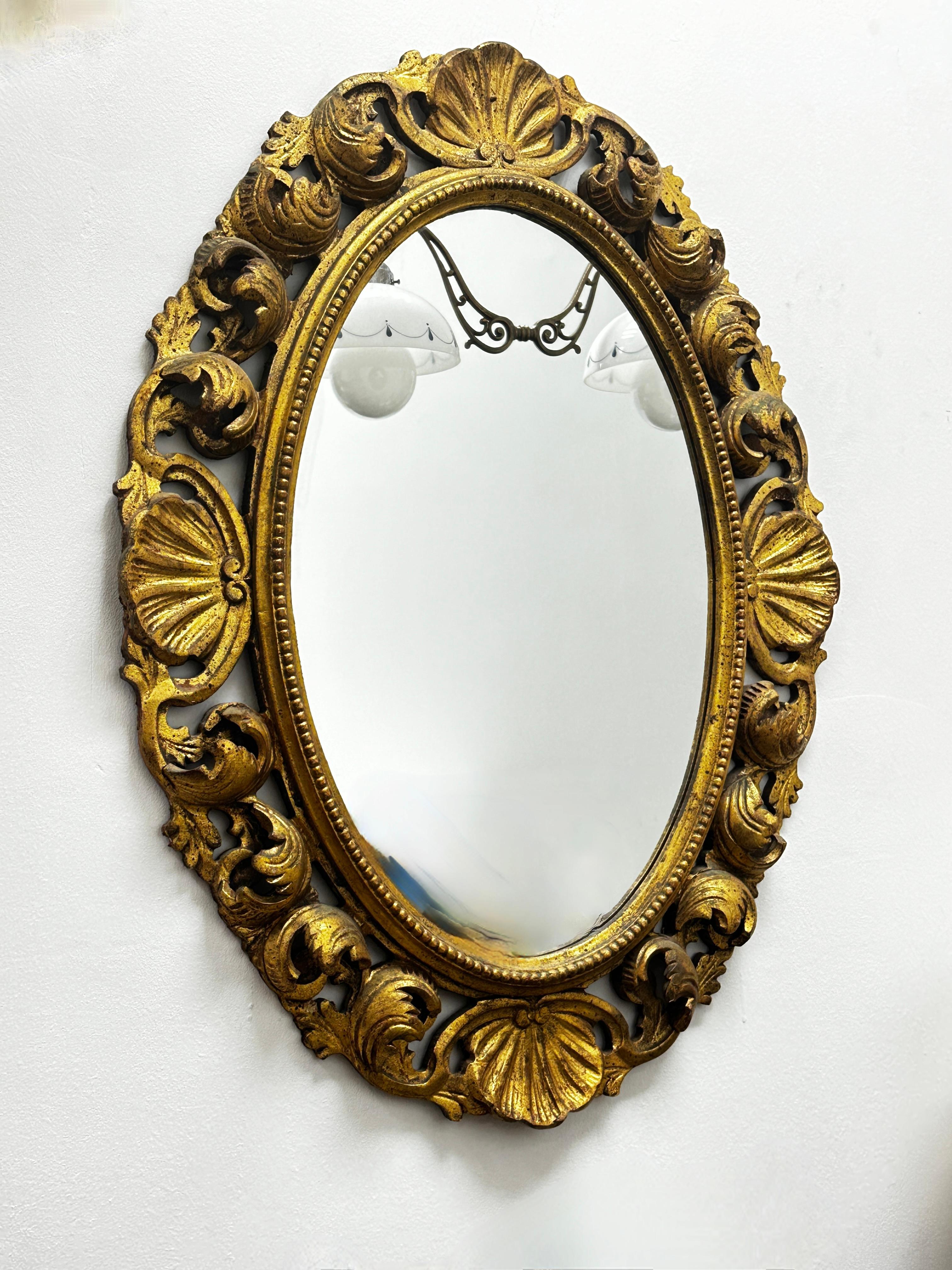 Stunning Hollywood Regency style toleware mirror. The gilt hand carved wooden frame surrounds a glass mirror. Viewable part of the Mirror itself measures approx. 21.5 inches high and 14.13 inches wide. Made in France, in the 1930s or older.