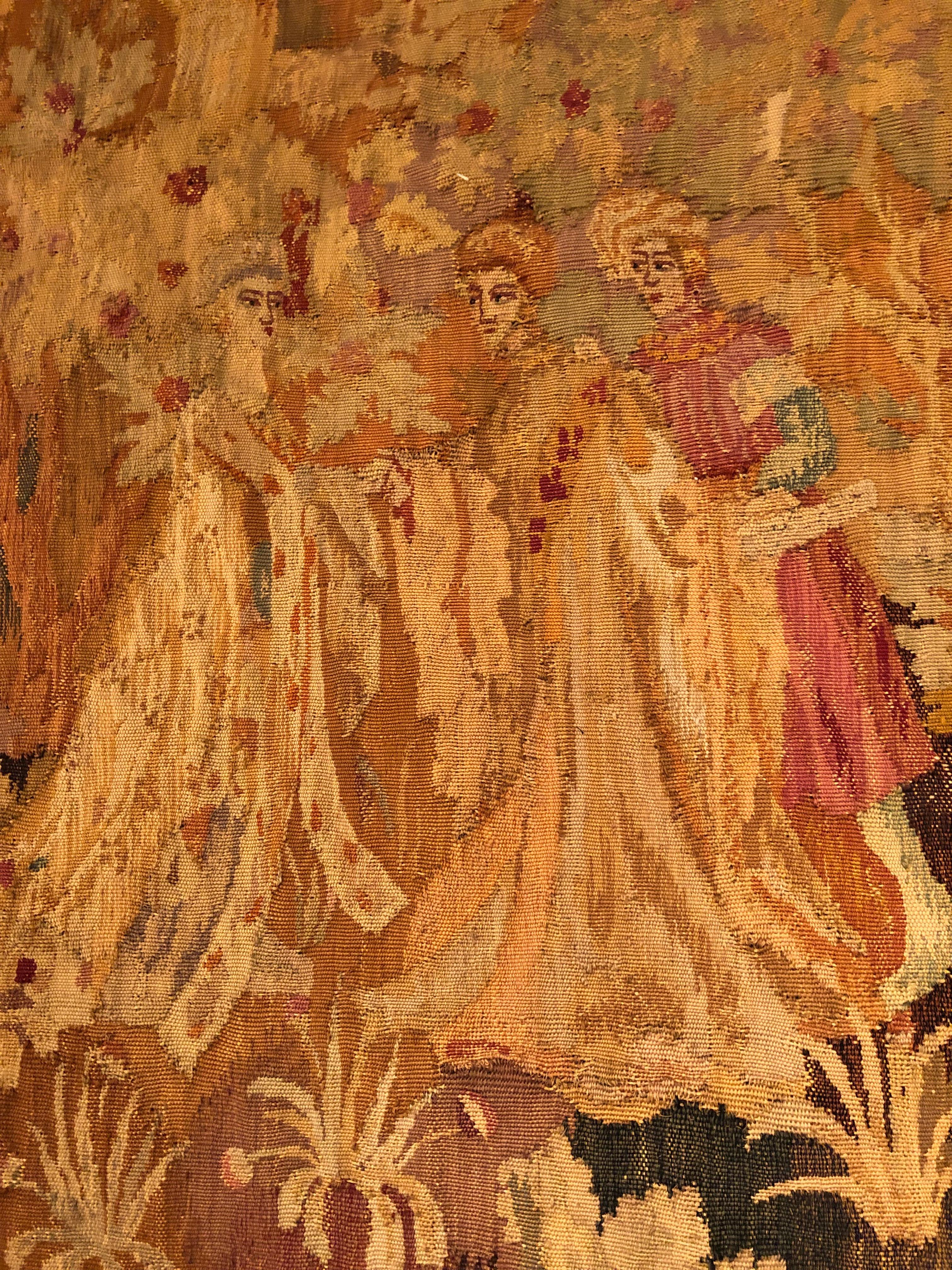 Gorgeous antique French tapestry in warm autumnal shades of gold, orange, brown and green depicting a royal group of ladies and gentlemen in the foliage in front of a stately castle. Exudes character and amber glow.
