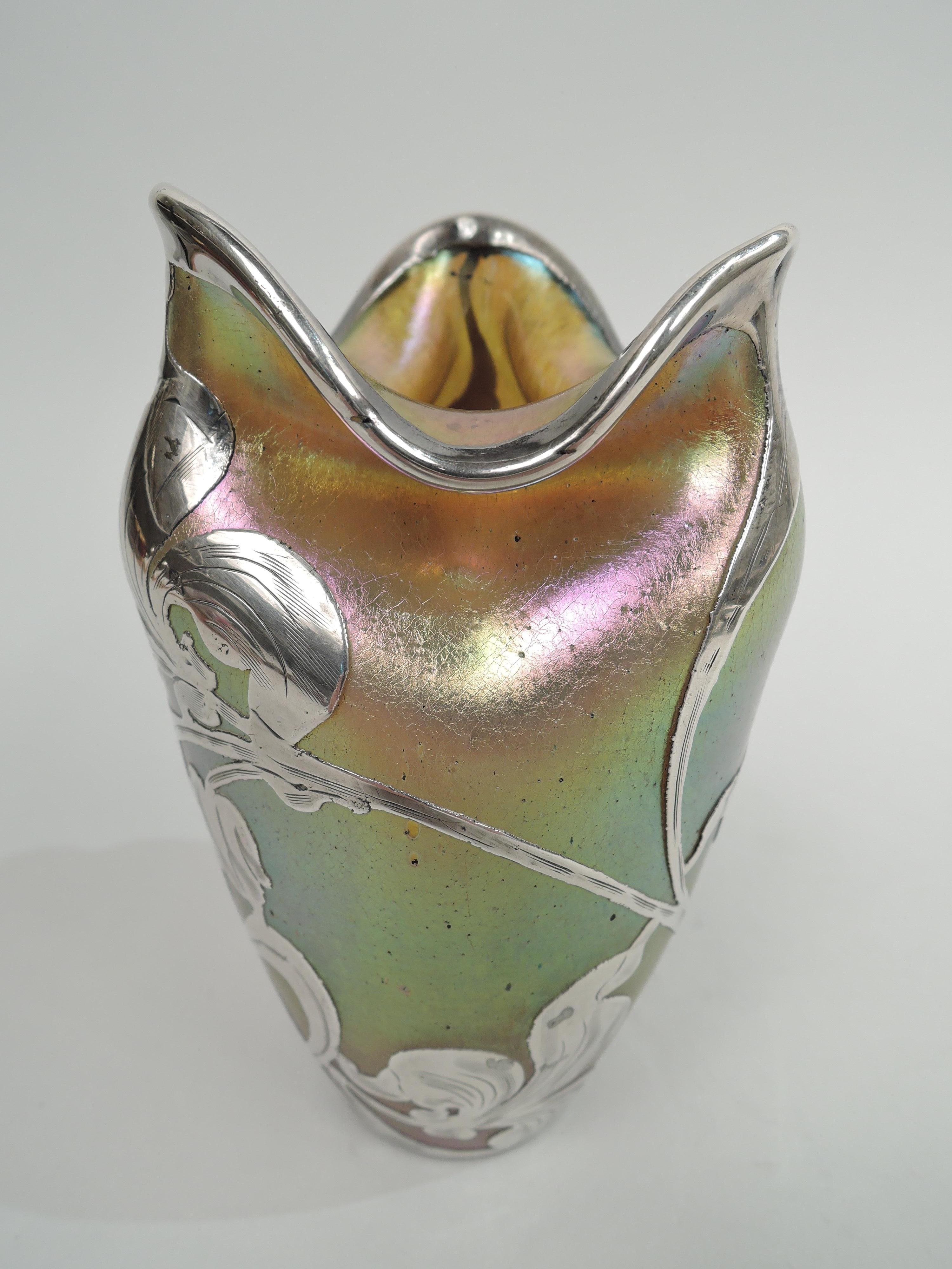 Turn-of-the-century silberiris glass vase by Loetz with engraved silver overlay. Ovoid with impressed shoulder and molten-style irregular turned-down rim. Overlay in form of whiplash tendrils and loose and fluid blooms. Glass iridescent in purple,