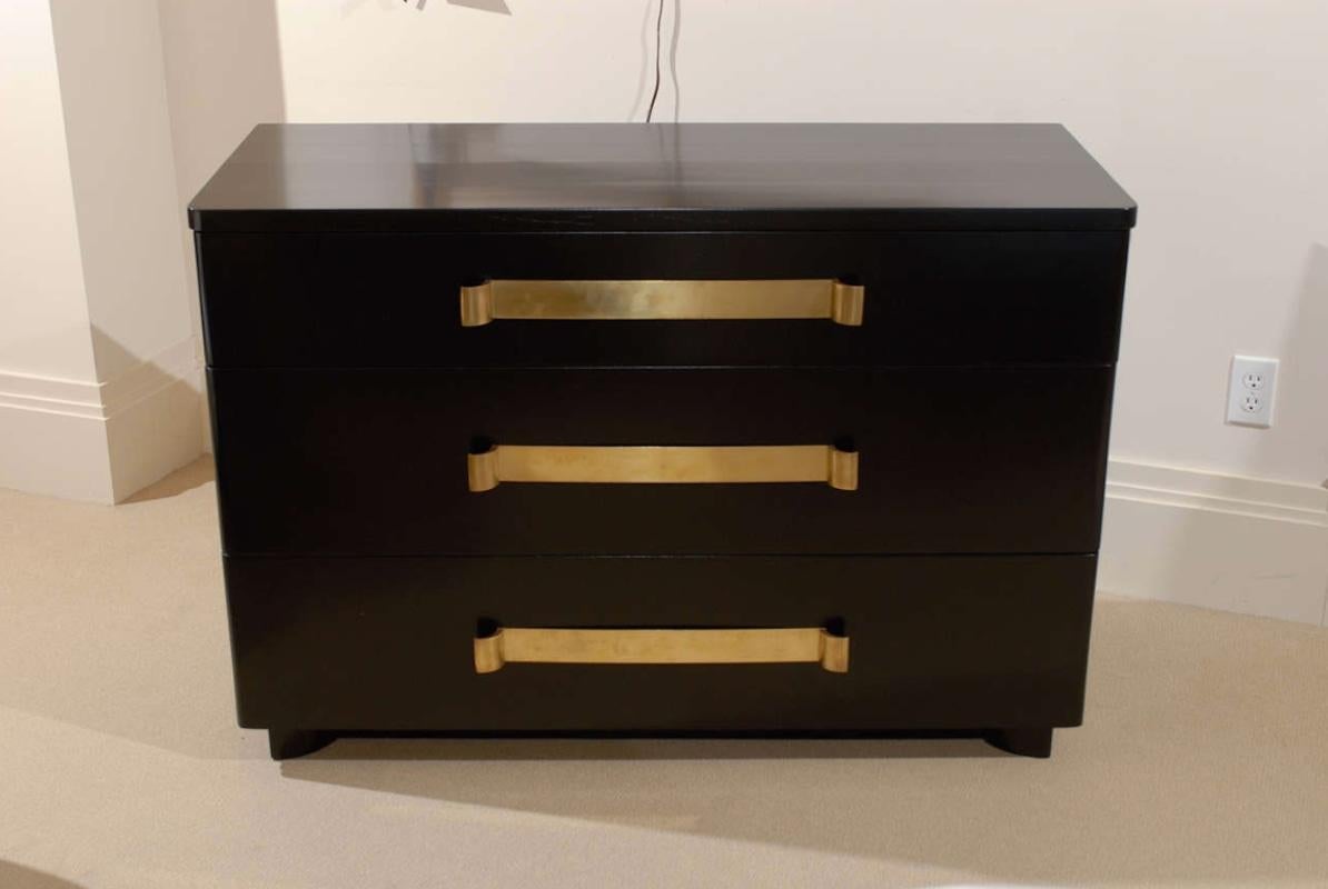 An exquisite restored Art Deco commode by John Stuart, circa 1940. Stout, expertly crafted mahogany case construction finished in black lacquer. Heavy elegant solid brass strap hardware mark the drawer fronts. An important focal point designed to