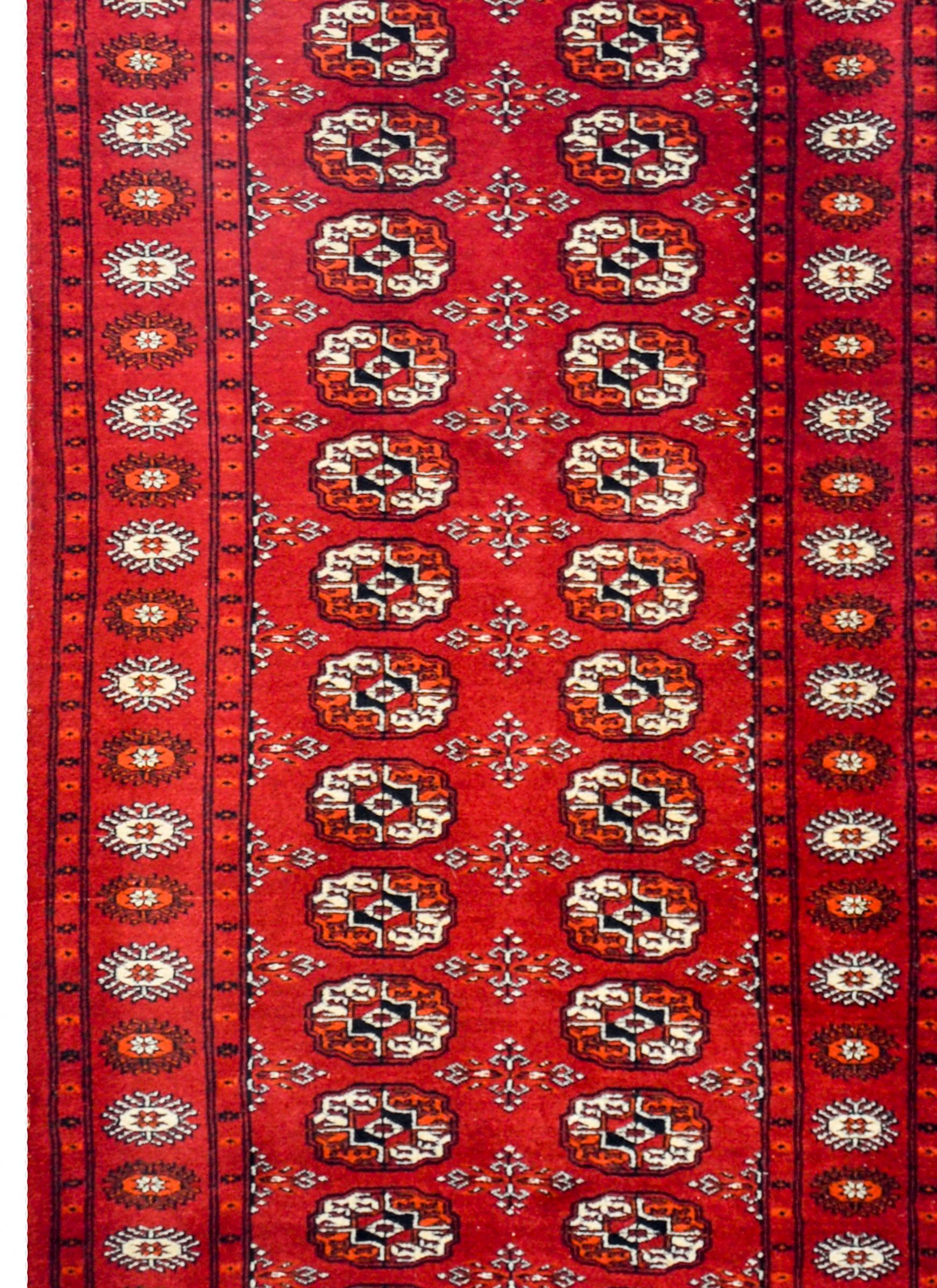 Ein pakistanischer Läufer aus dem frühen 20. Jahrhundert mit einem stilisierten Blumenmuster, gewebt aus orangefarbener und weißer Wolle, auf einem Hintergrund in intensiven Karminrotfarben. Die Bordüre ist wunderschön, mit einem abwechselnden