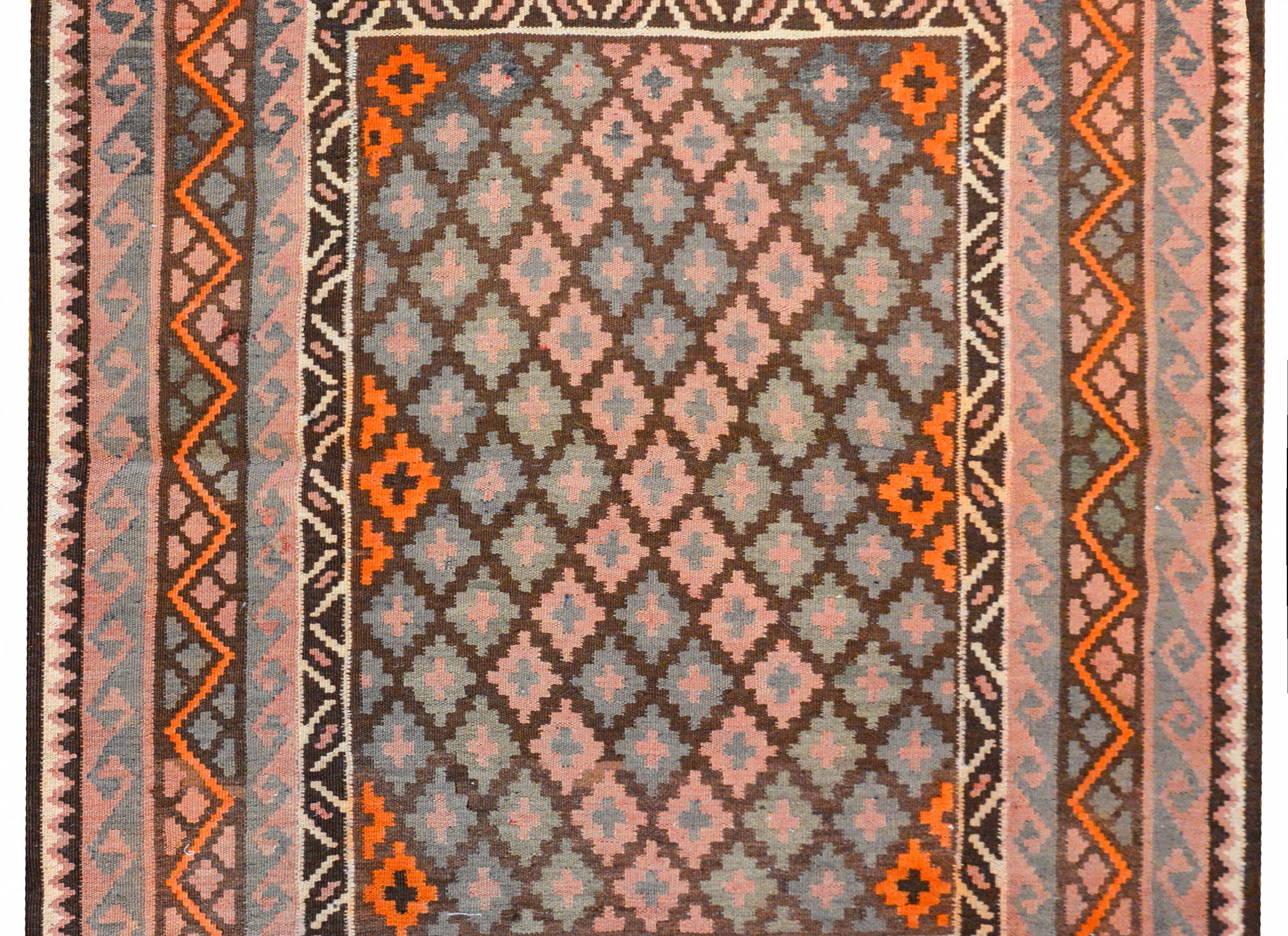 A gorgeous mid-20th century Afghani kilim with an all-over diamond pattern woven in pale indigo, green, orange, and pink vegetable dyed wool, surrounded by a complex border containing a Grecian wave pattern, with zigzags and triangles, all woven in