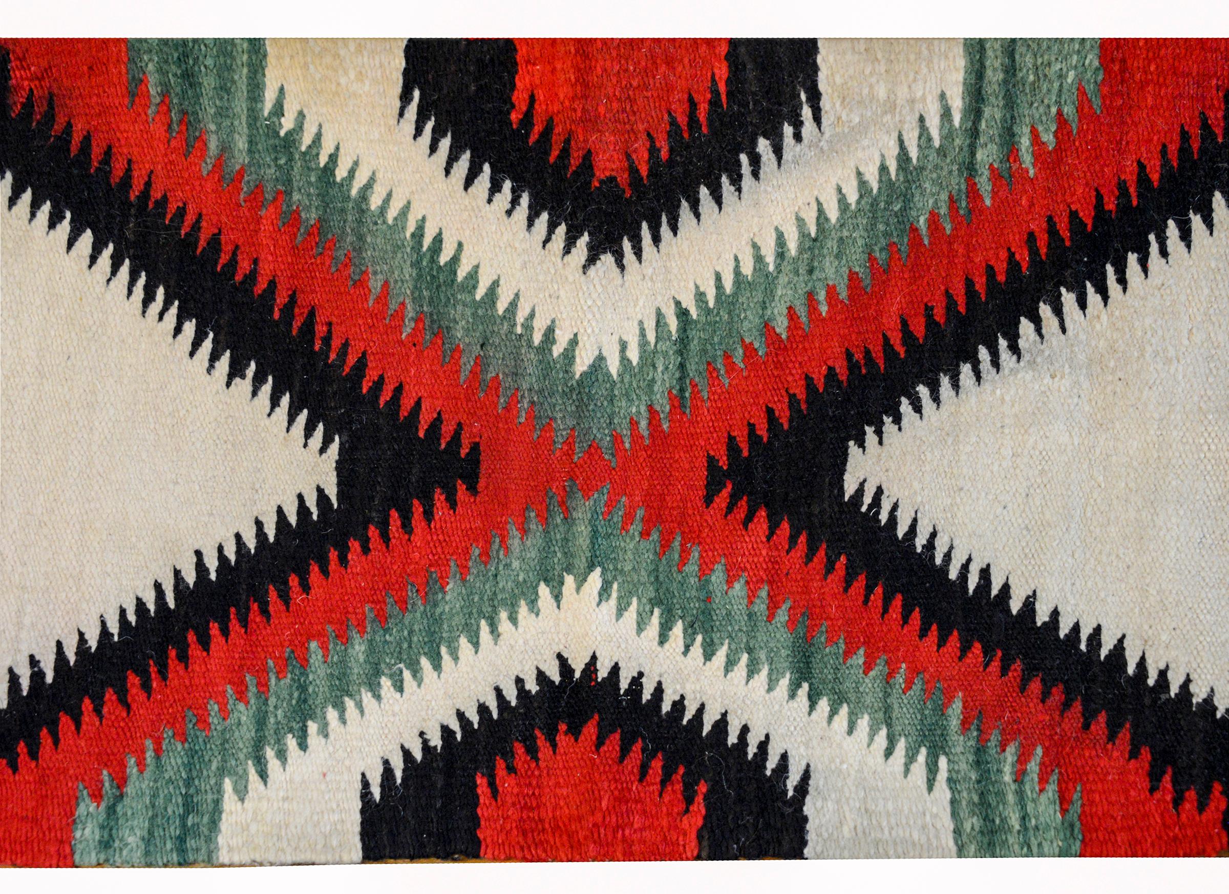 A gorgeous mid-20th century Navajo rug with a bold large-scale cross woven in crimson, black, and sea-foam green, against a cream colored background.