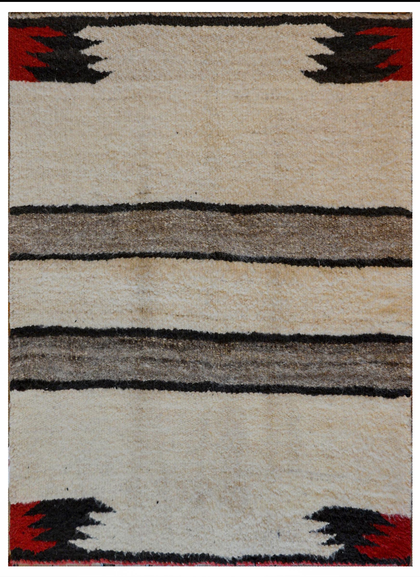 A gorgeous early 20th century Navajo rug with a natural cream wool background with two wide gray and black stripes in the center, and red and black zigzag patterned motifs in each of the corners.