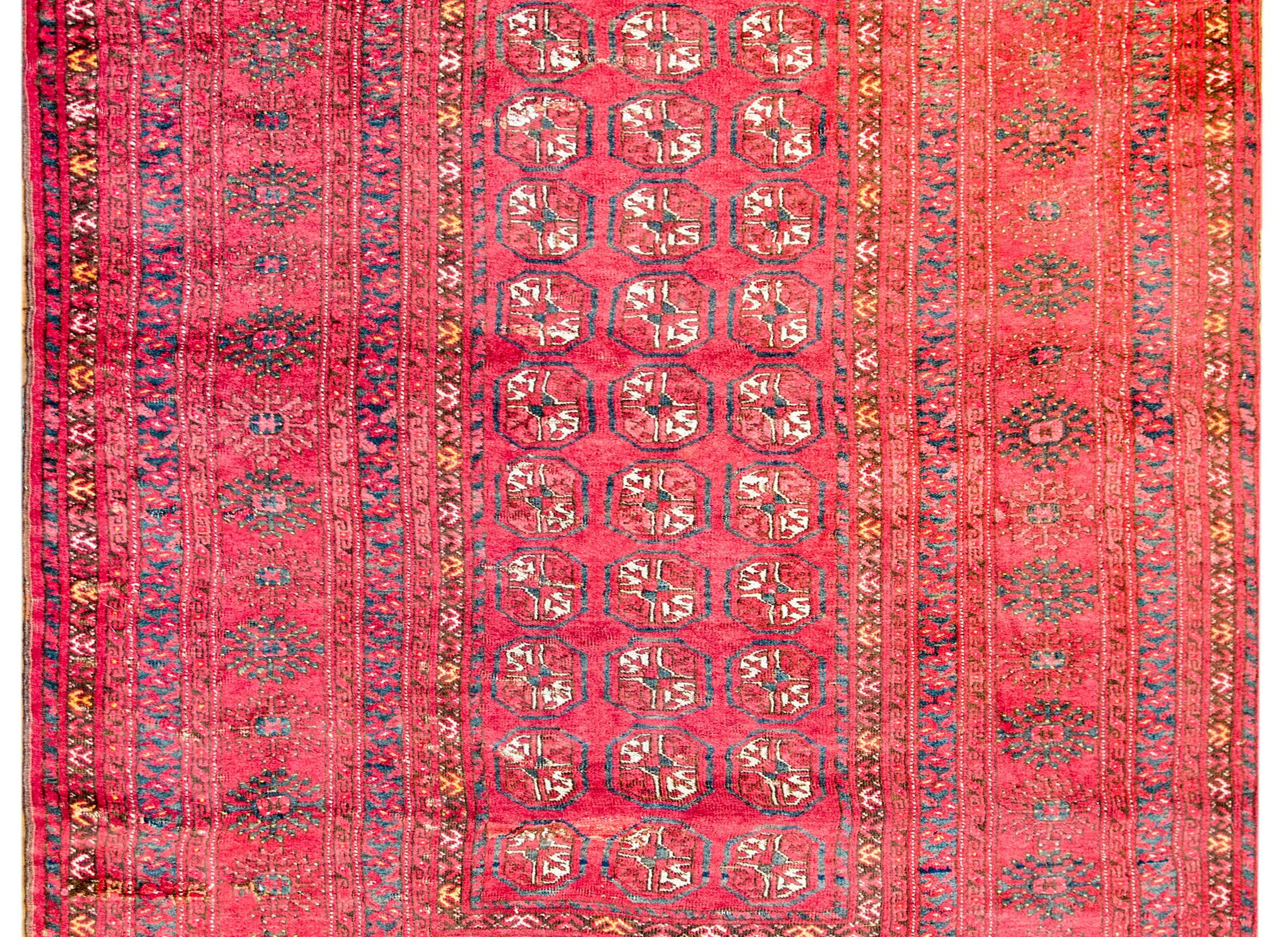 A gorgeous vintage Turkmen rug with an all-over pattern of small medallions woven in orange, white, and indigo vegetable dyed silk on a brilliant crimson background. The border is exceptionally wide with a large central stylized floral stripe