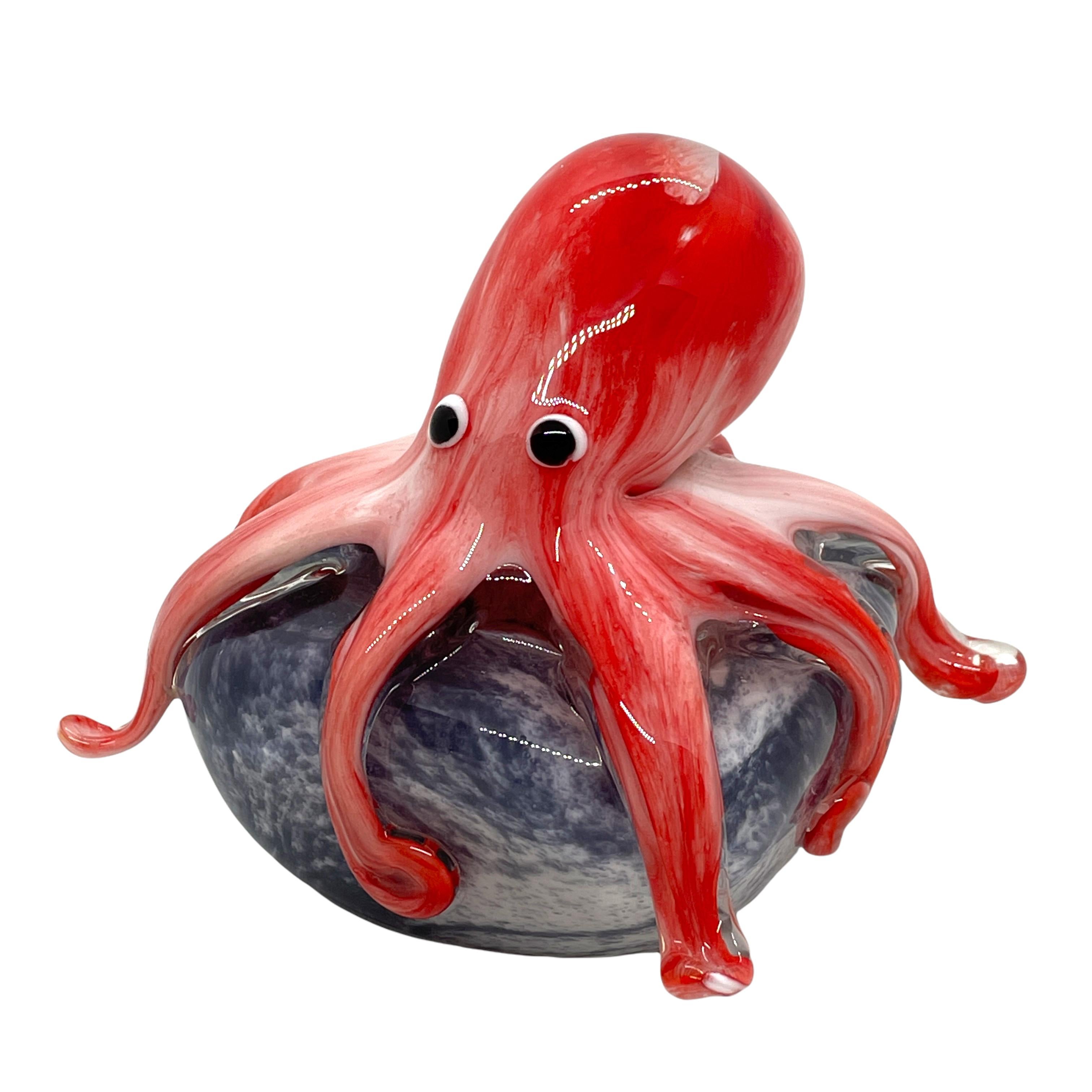 Beautiful Murano hand blown aquarium Italian art glass paper weight. Showing a giant octopus, on a glass stone. Colors are a red, grey, white, black and clear. A beautiful nice addition to your desktop or as a decorative piece in every room.