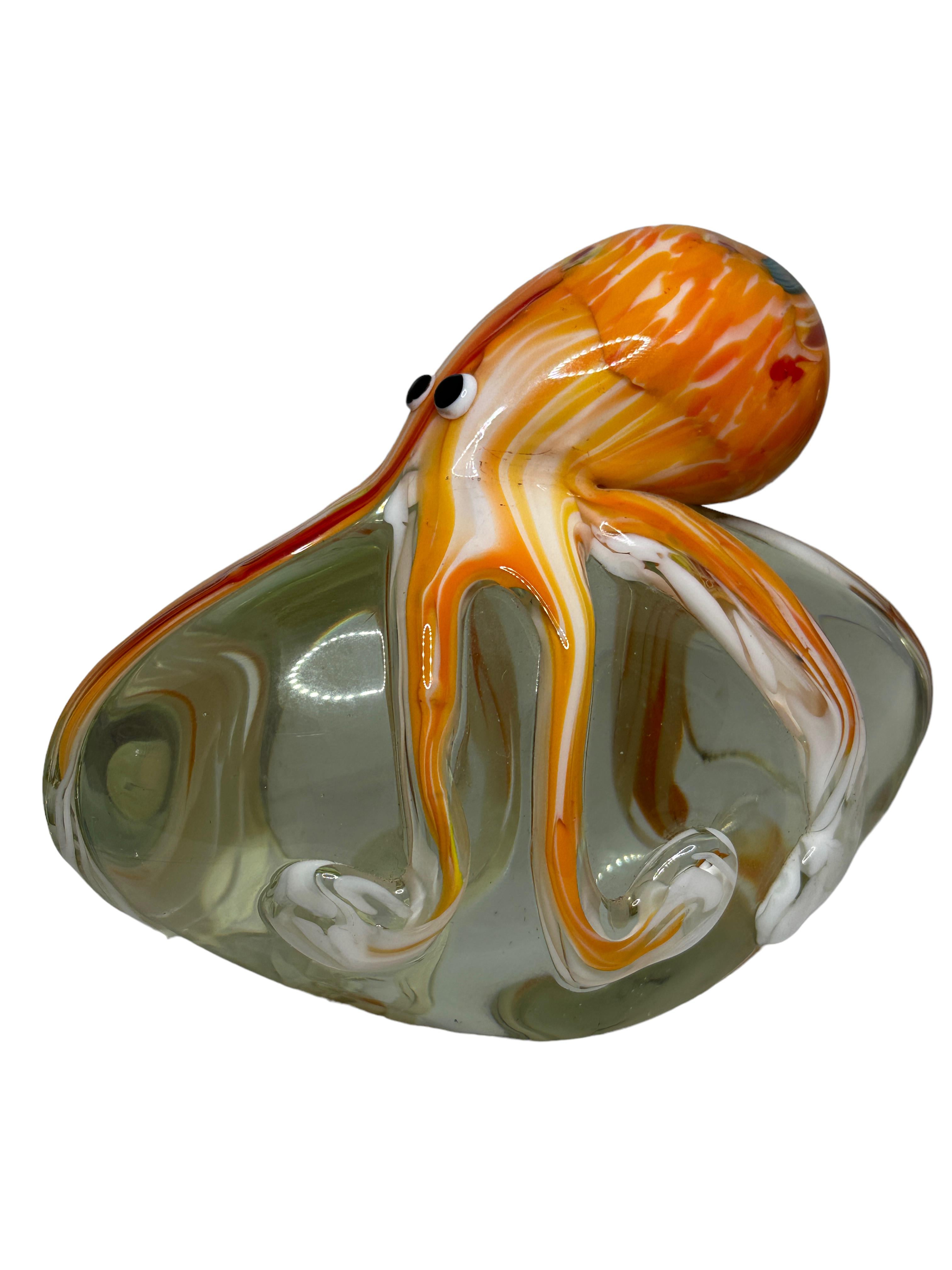 Beautiful Murano hand blown aquarium Italian art glass paper weight. Showing a giant octopus, on a glass stone. Colors are an orange, red, white, blue and clear. A beautiful nice addition to your desktop or as a decorative piece in every room.