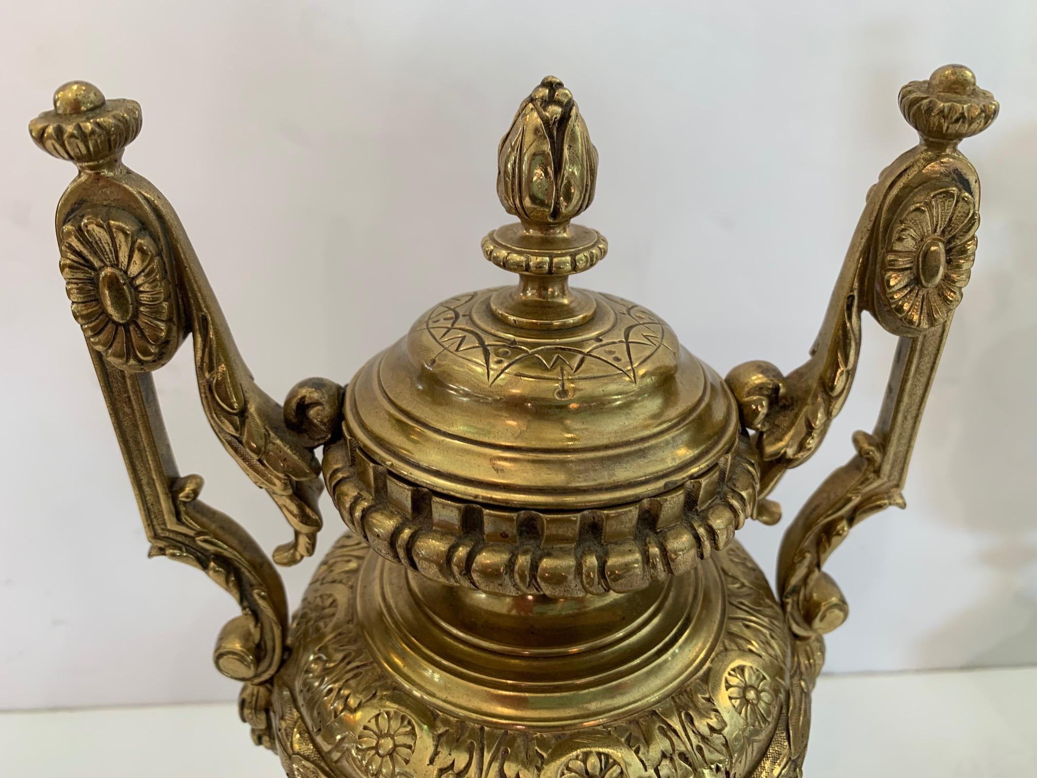 Pair of Classical Revival style continental relief cast brass double-handled covered urns having rosette and scroll handles with dental molded frame top finial lid over a relief cast body of scrolling grapevines and grapes, raised on a stepped foot