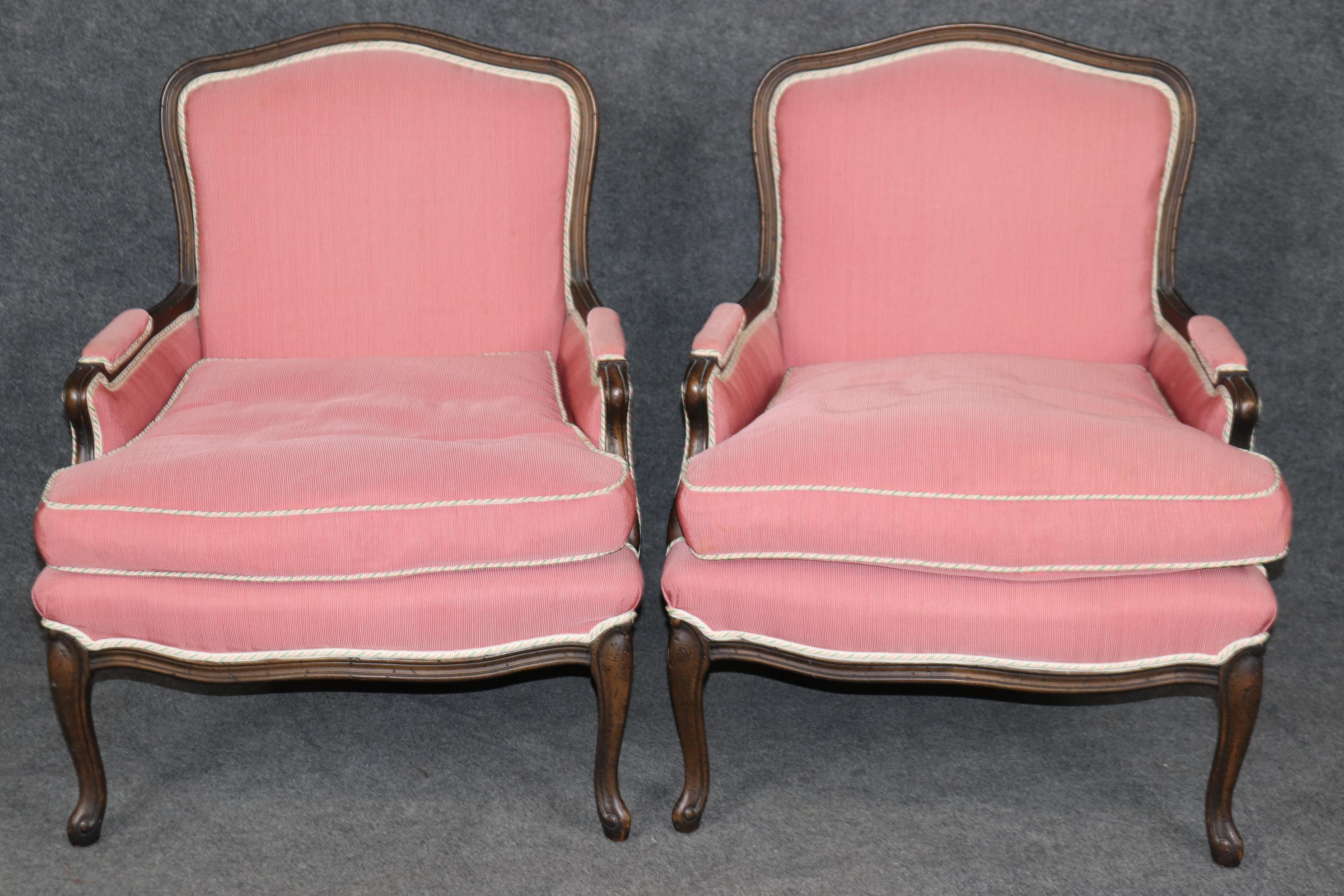 This is a stunning and sophisticated pair of French carved distressed finished walnut bergere chairs with superb pink, off-white trim and green candy-cane piping. The chairs are in good original condition with beautiful upholstery. The chairs are in