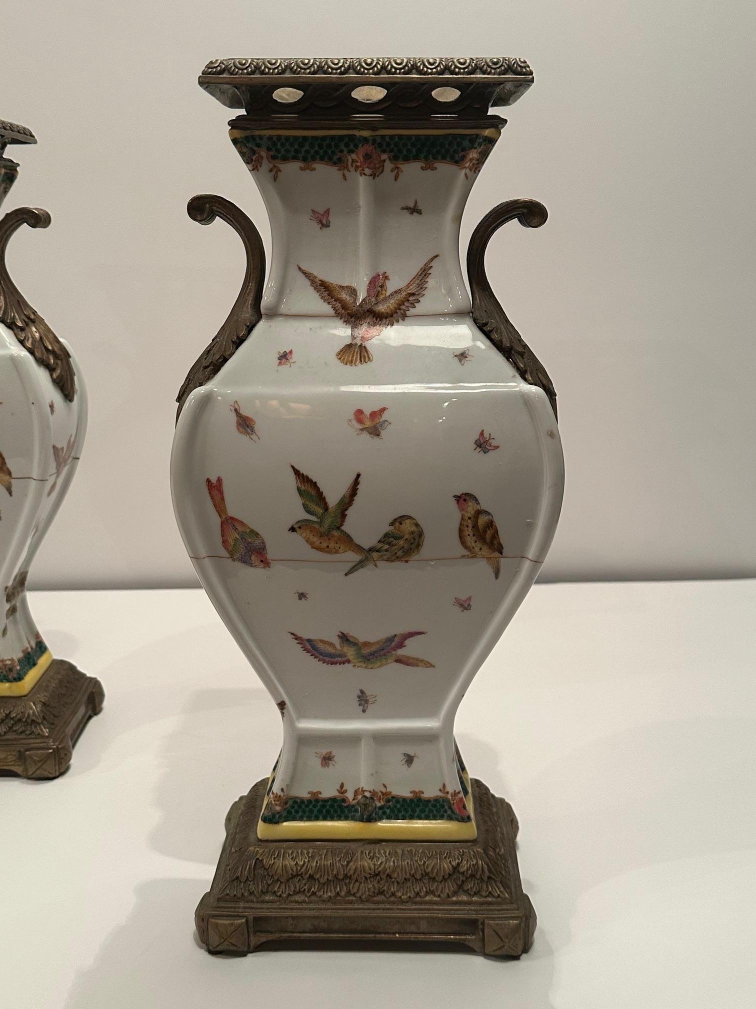 Elegante pareja de jarrones de estilo francés con monturas de bronce y preciosa porcelana decorada con pájaros y mariposas.