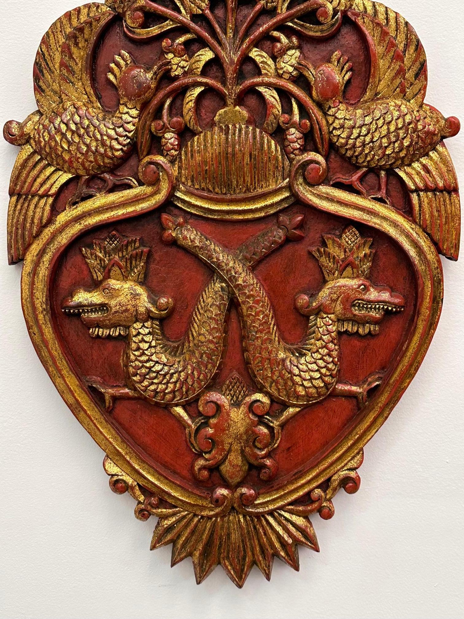 Striking pair of shield shape hand carved wall plaques having red underpaint and gilding with ornate decoration.