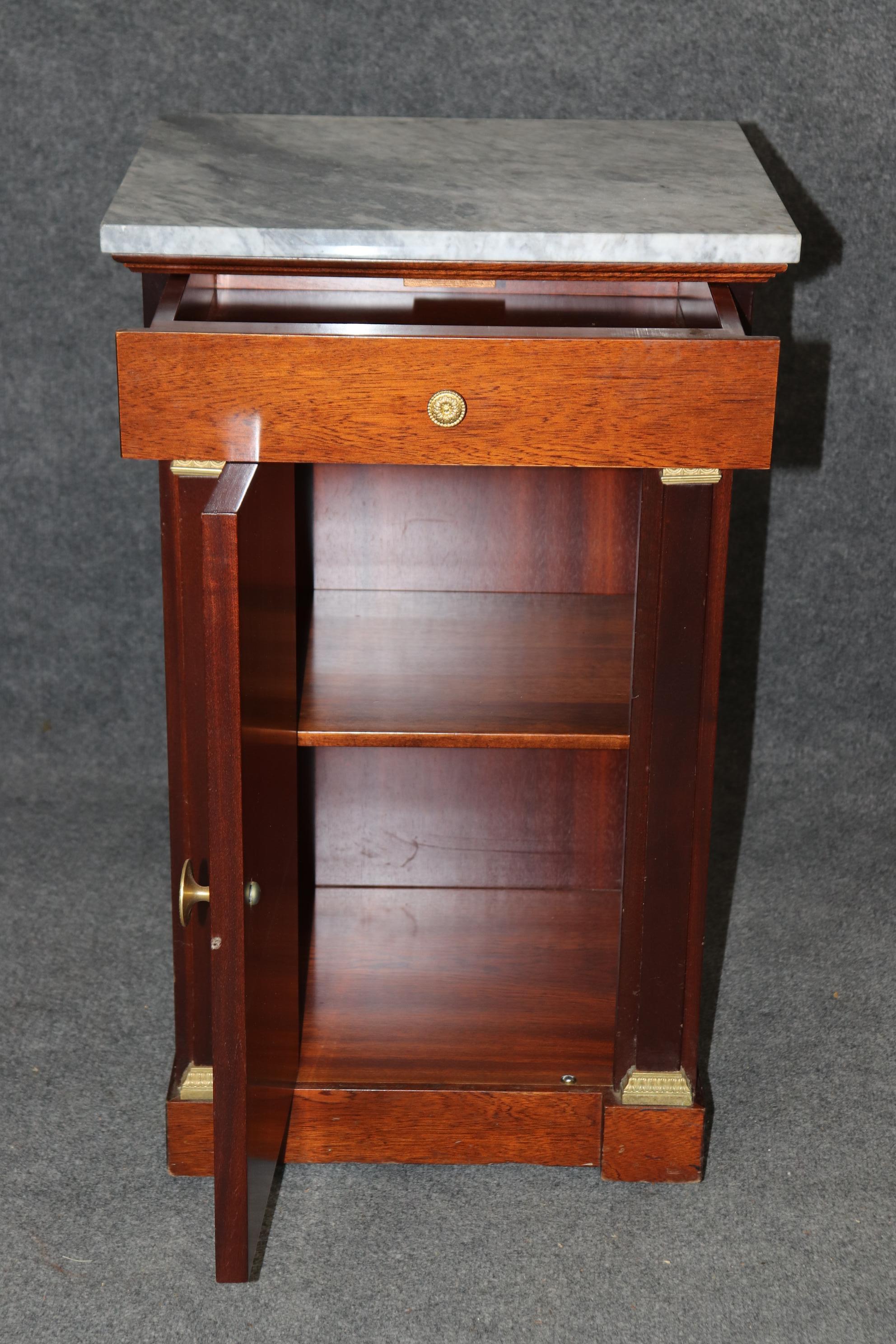 This is a gorgeous pair of 1950s era French-made Empire style nightstands or commodes that feature gorgeous dore' gold gilded bronze mounts and hardware and beautiful varigated marble tops. The stands are solid mahogany and dove-tailed drawer