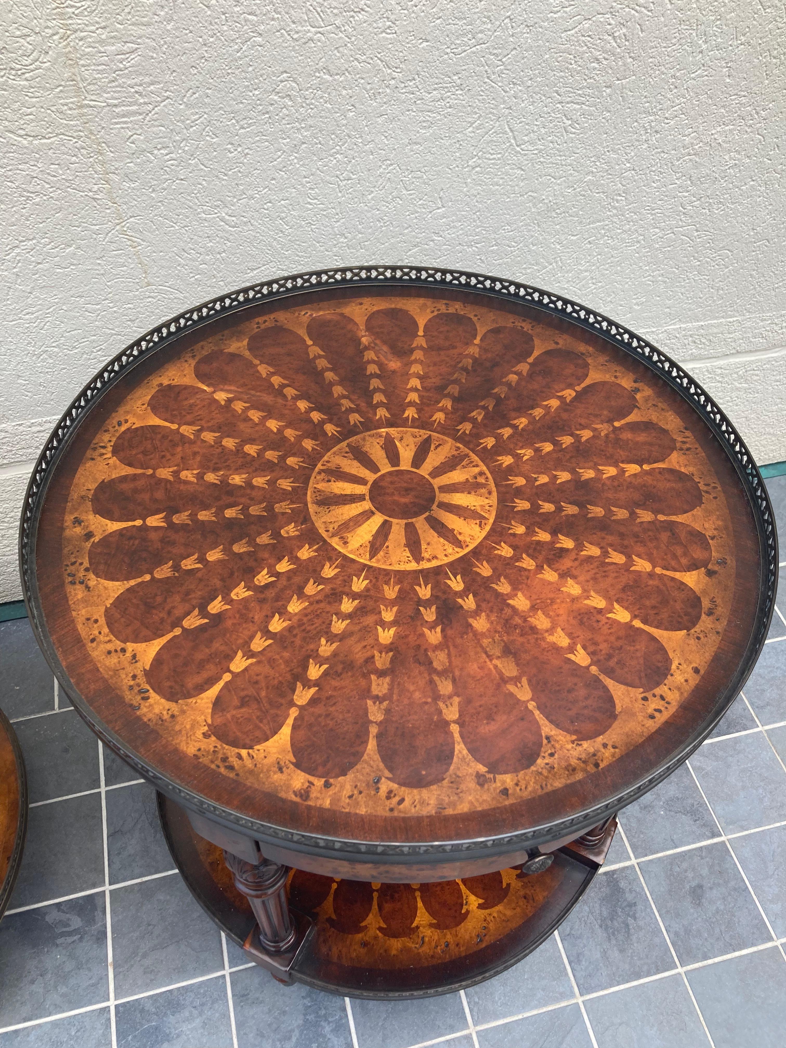 A gorgeous pair of substantial round two tier burl side tables, one heavily inlaid and the other plain. Each has a patinated brass pierced gallery and similar undertier with single drawer and handsome carved legs.

Note: Will split the set for